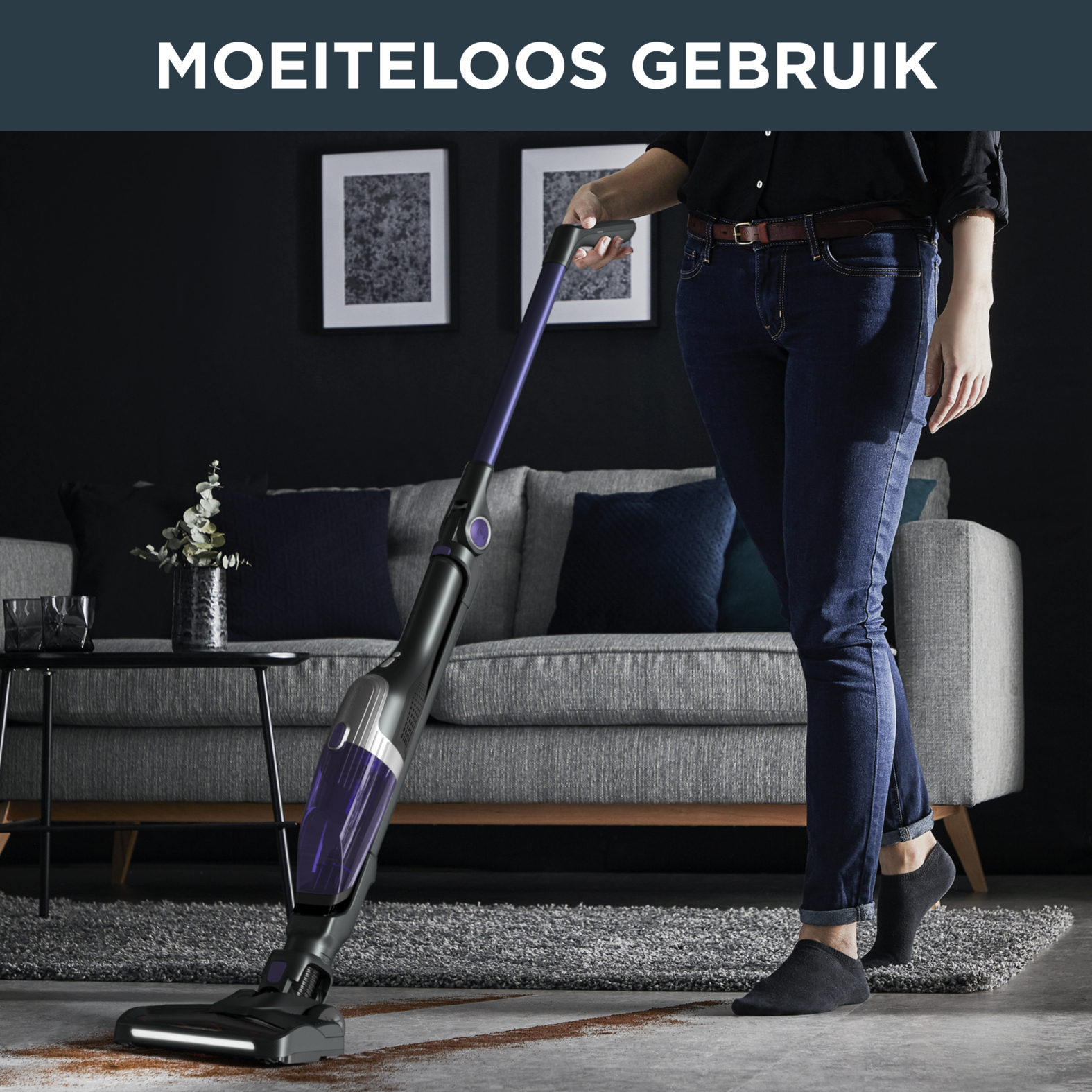 Een vrouw die een tapijt stofzuigt met een paarse en zwarte stofzuiger.