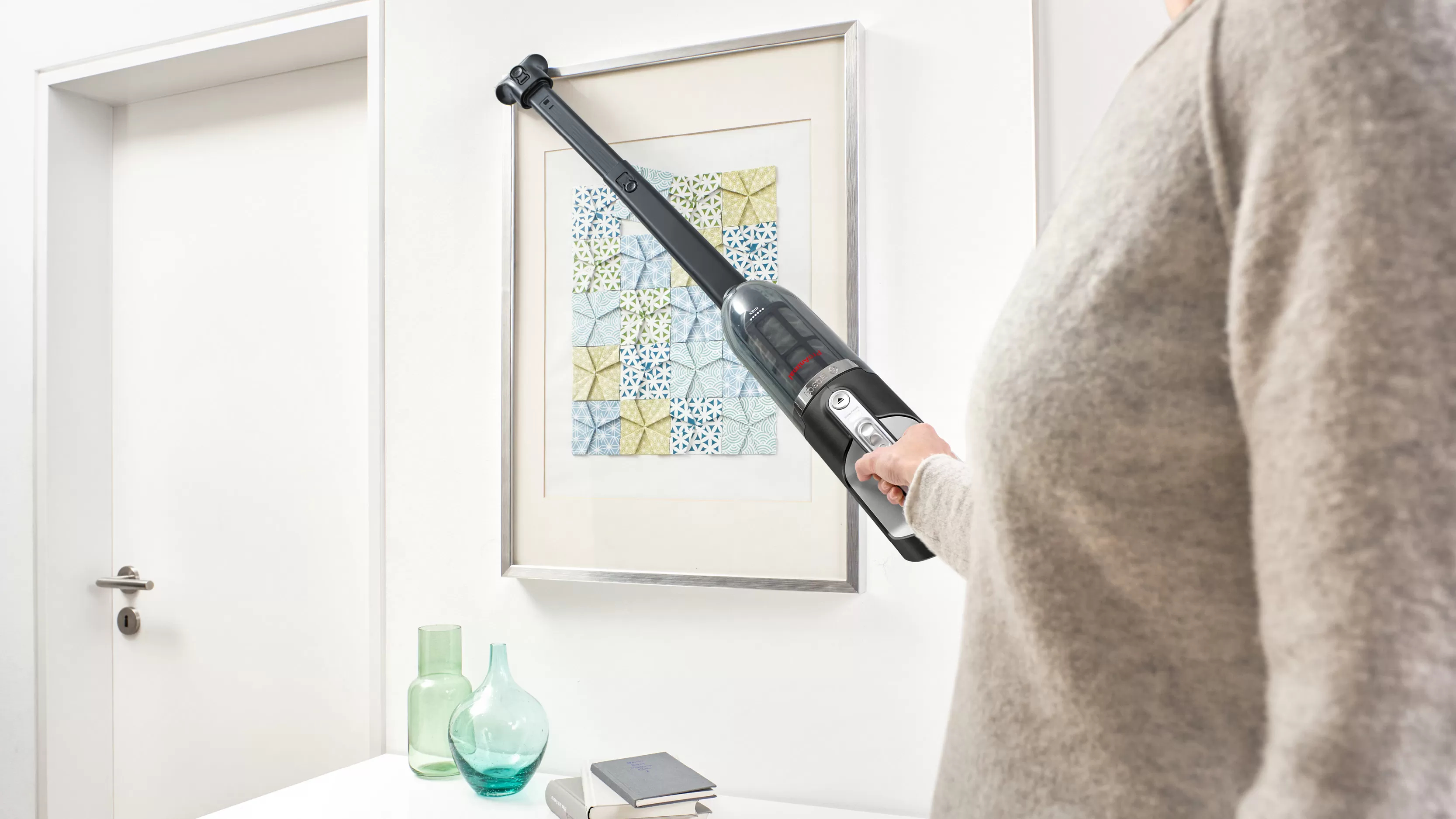 Kobieta używająca odkurzacza na ramie obrazu wiszącej na białej ścianie.