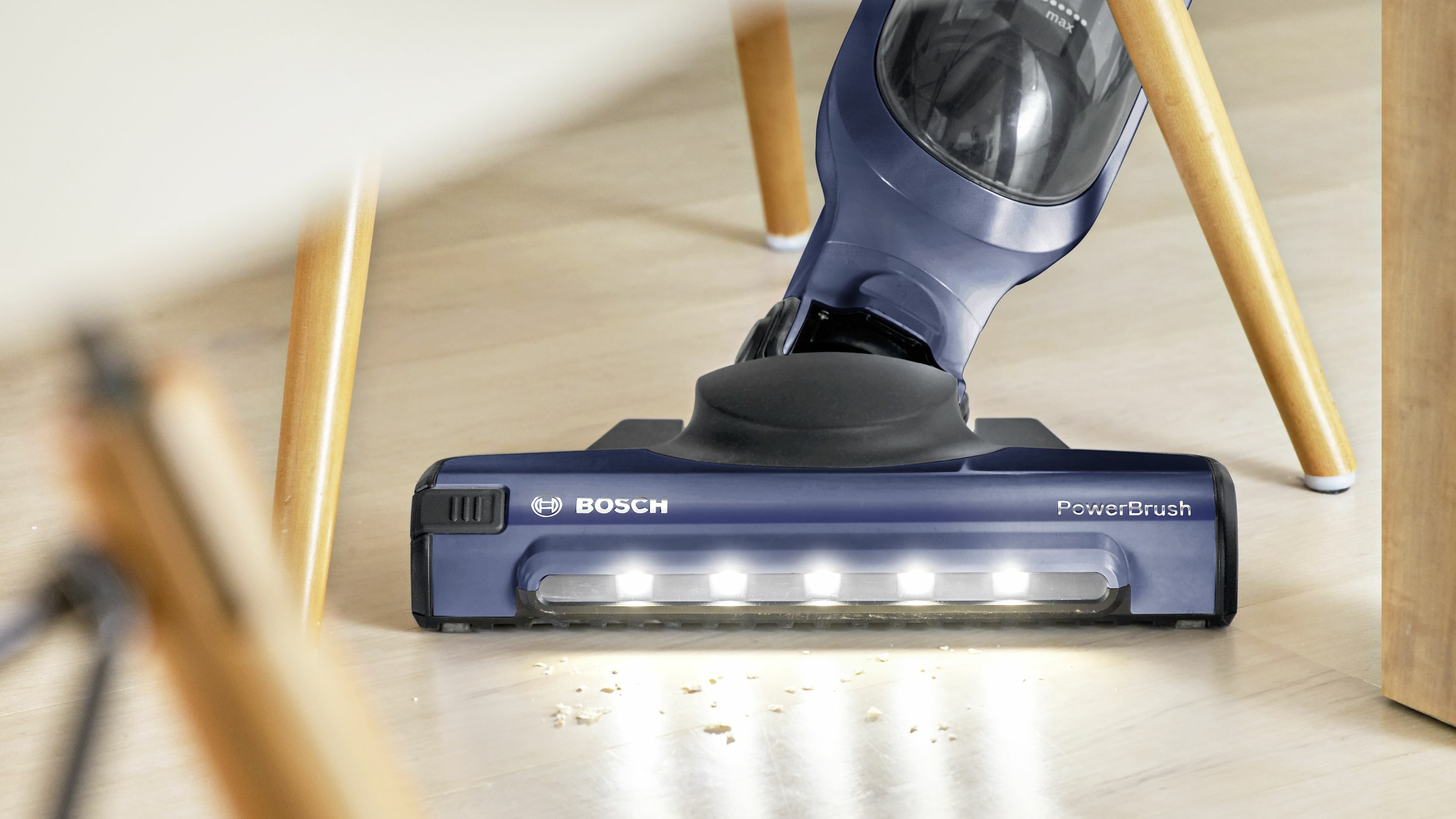 Un primer plano de un cabezal de aspiradora inalámbrica azul con luces, sobre un piso de madera.