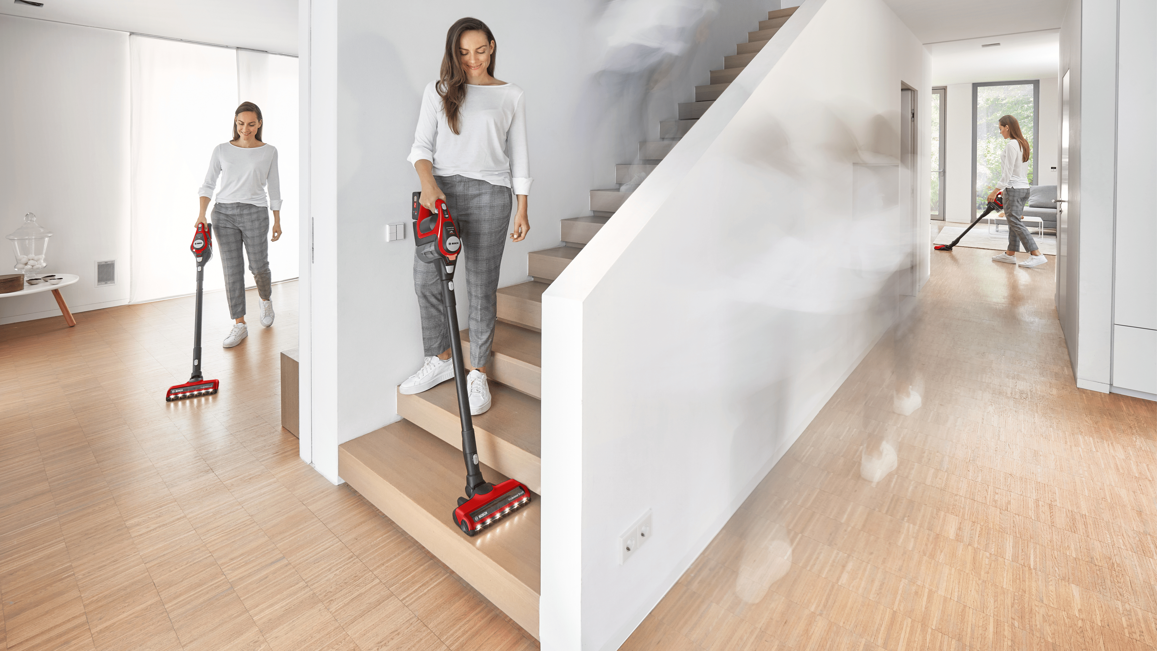 Frau, die Treppen und Boden saugt. Eine andere Frau im Hintergrund. Der Staubsauger ist rot und schwarz.