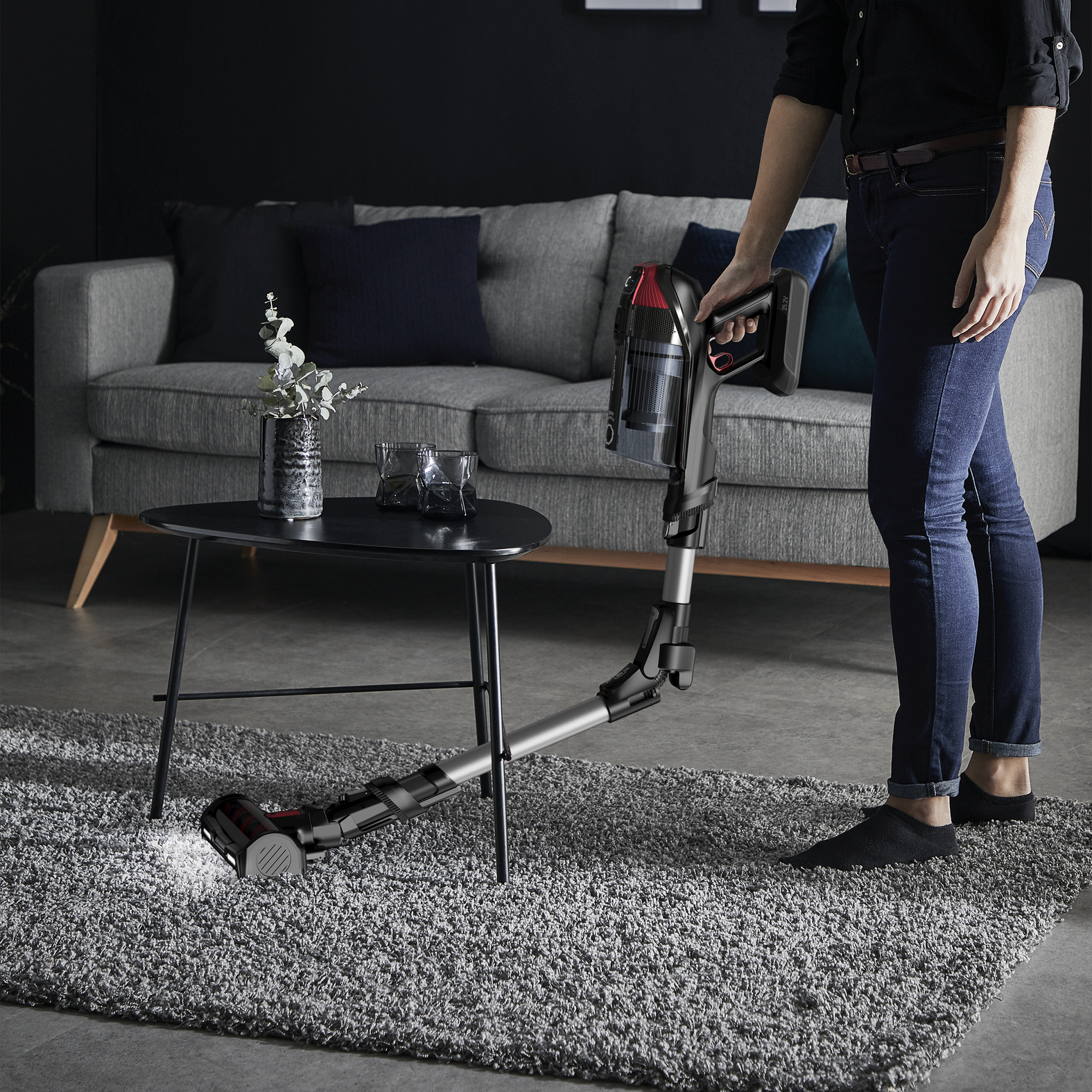 Una persona aspirando una alfombra con una aspiradora inalámbrica en una sala de estar.