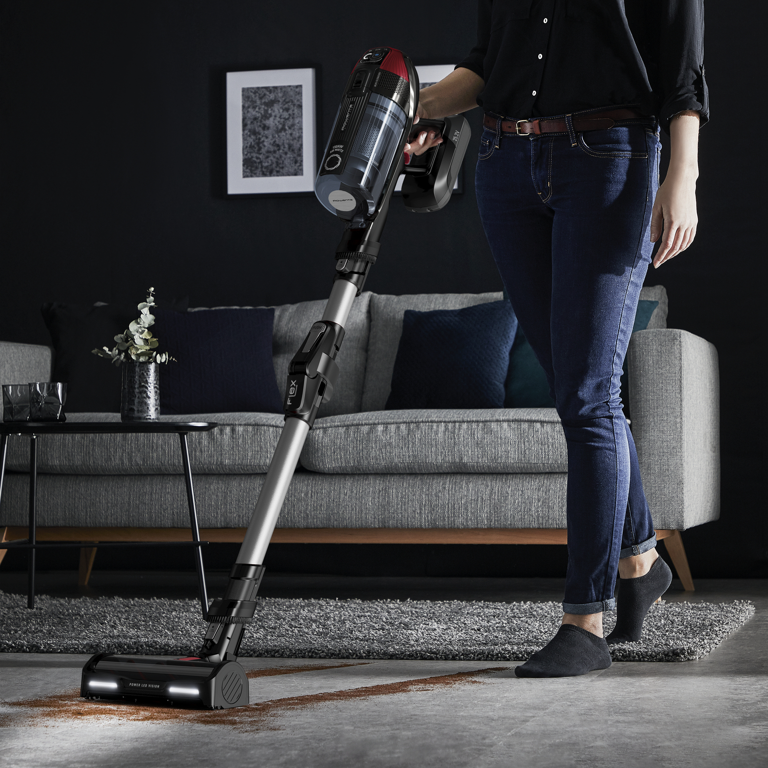 Una mujer aspirando una sala de estar con una aspiradora negra y plateada.