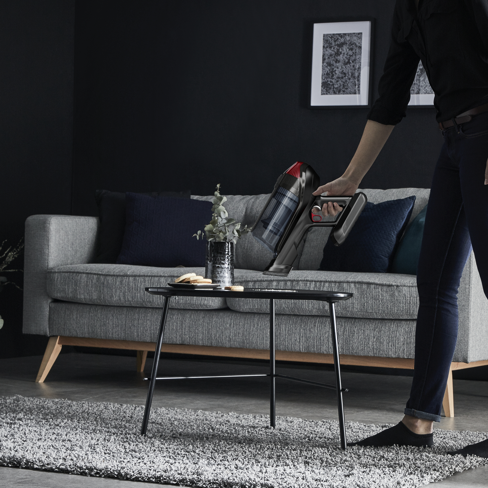 Mujer aspirando una sala de estar. Sofá gris, mesa negra con decoración.