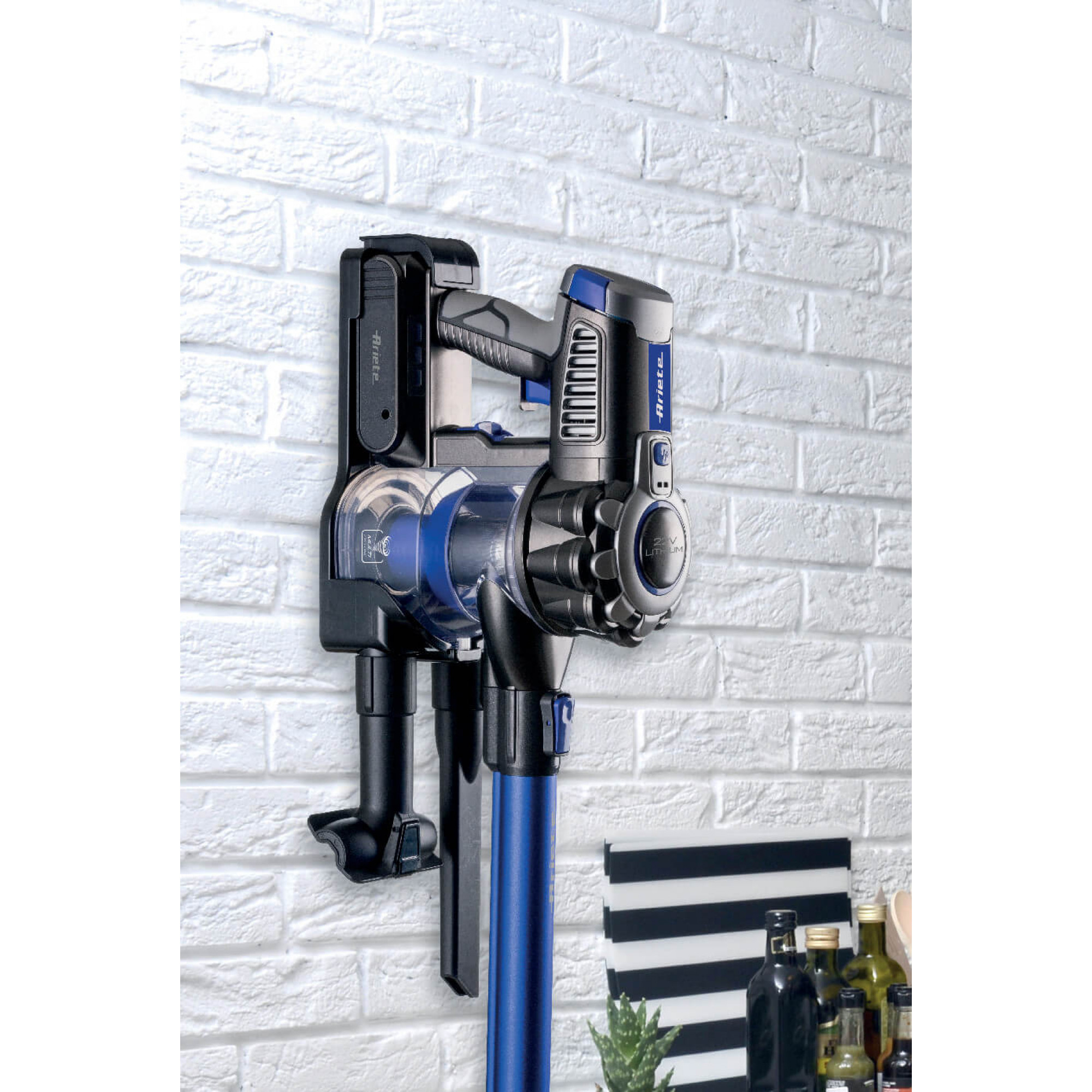Aspirapolvere senza filo montato su un muro di mattoni bianchi. Design nero e blu.