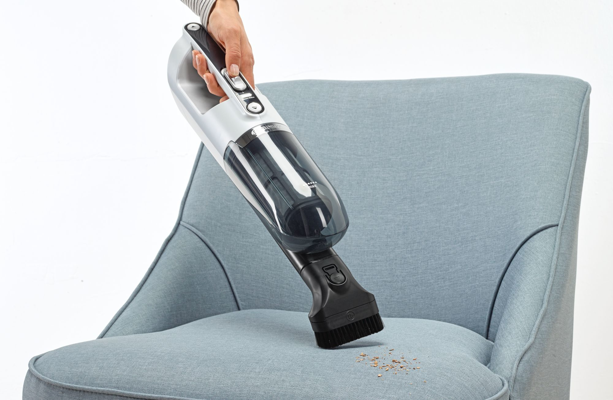 Una persona usa una aspiradora de mano en un sillón azul. Algunos escombros en la silla.
