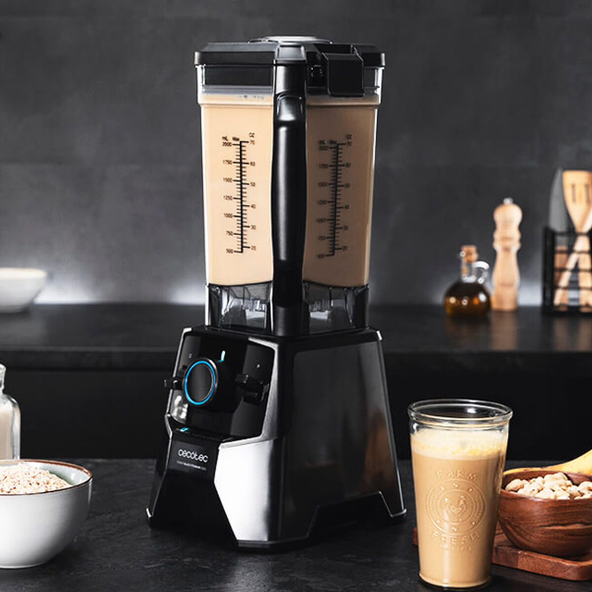 Una licuadora negra y plateada con dos recipientes llenos de líquido beige y un vaso con bebida.