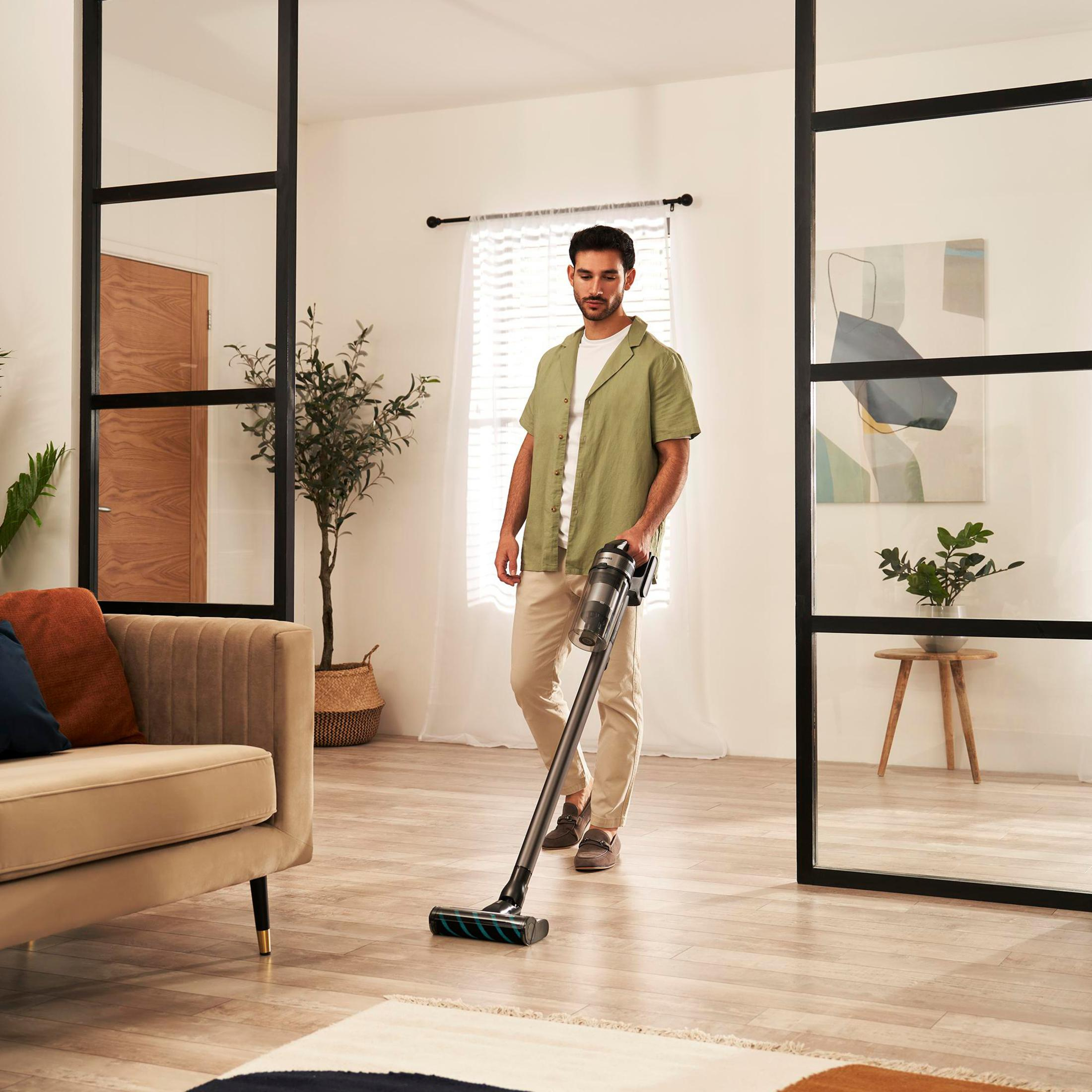 Uomo che aspira un pavimento in legno. Mostra un divano, porte in vetro e una pianta sullo sfondo.