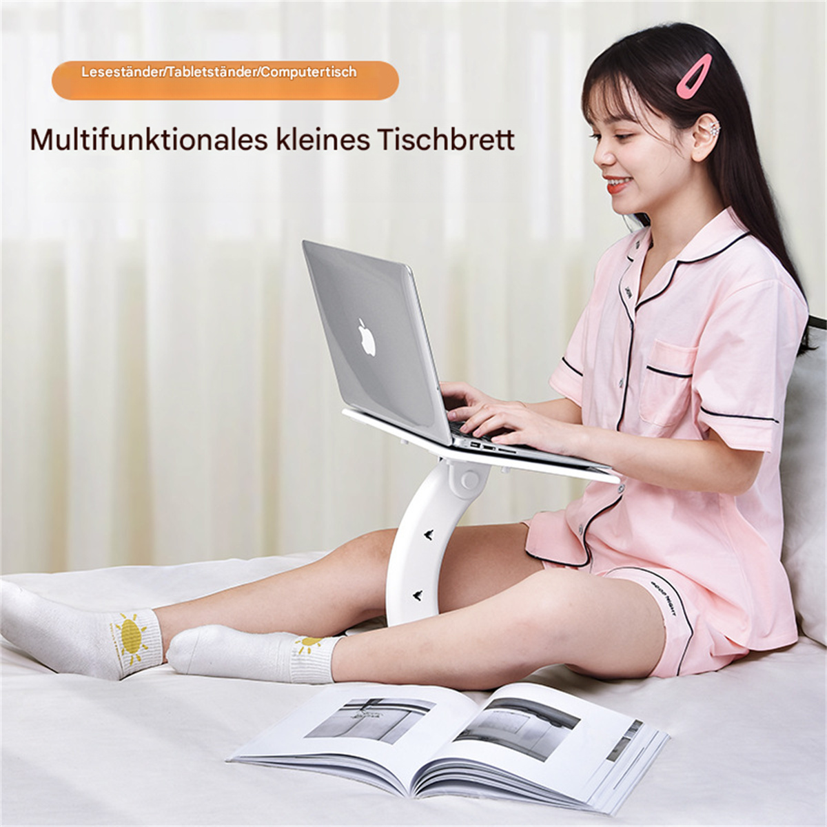Frau in rosa Pyjama, die einen Laptop auf einem weißen Ständer benutzt, während sie auf einem Bett sitzt.