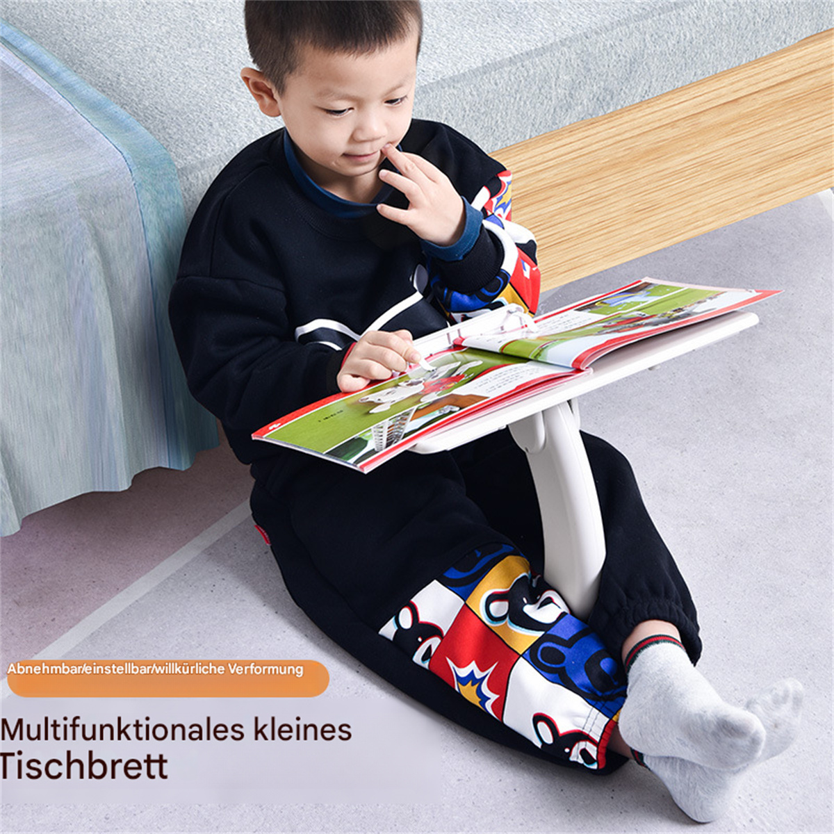 Ein junger Junge liest ein Buch auf einem kleinen weißen Schreibtisch, der auf einem Teppich auf dem Boden sitzt.