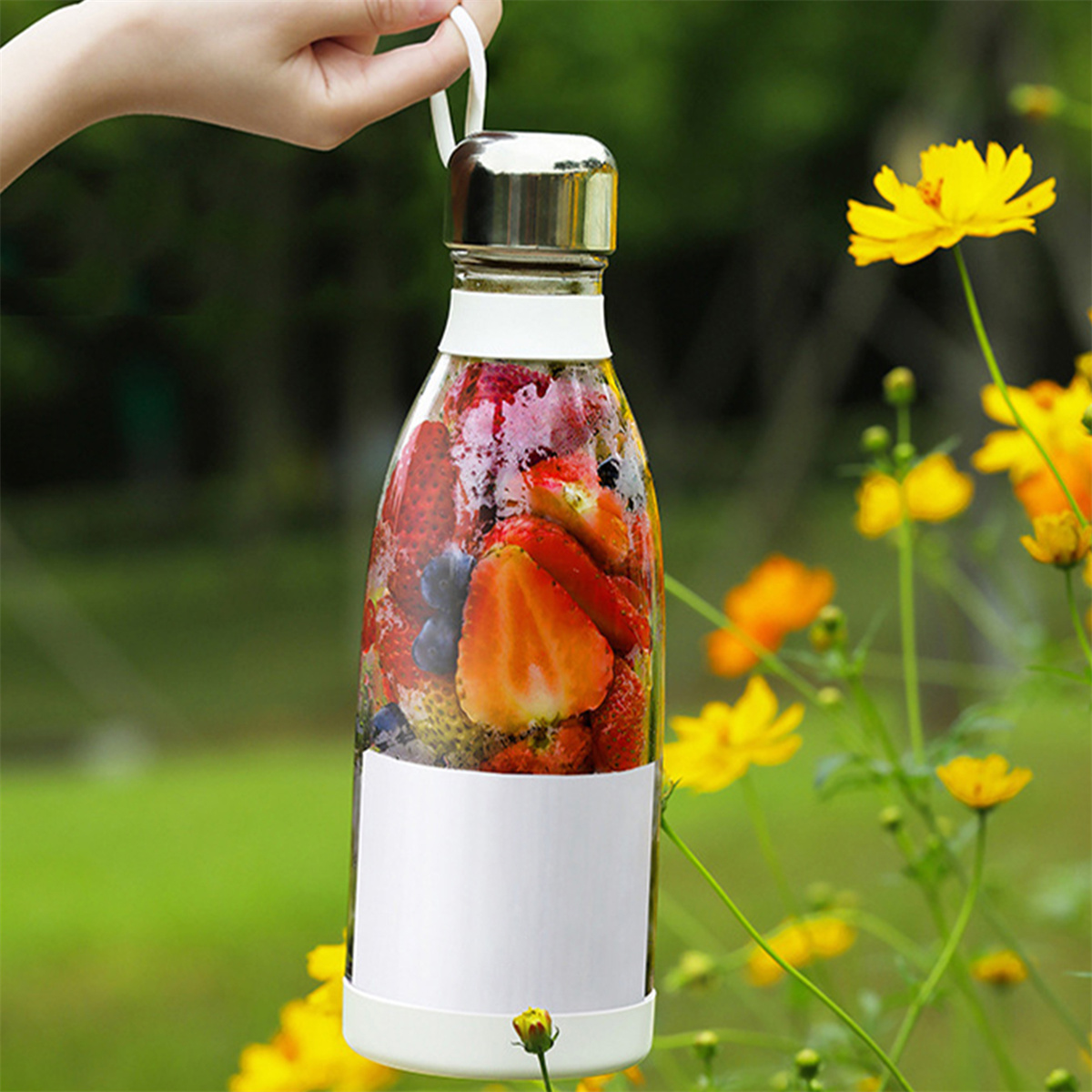 Eine Hand, die einen tragbaren Mixer mit Erdbeeren und Blaubeeren im Freien hält.