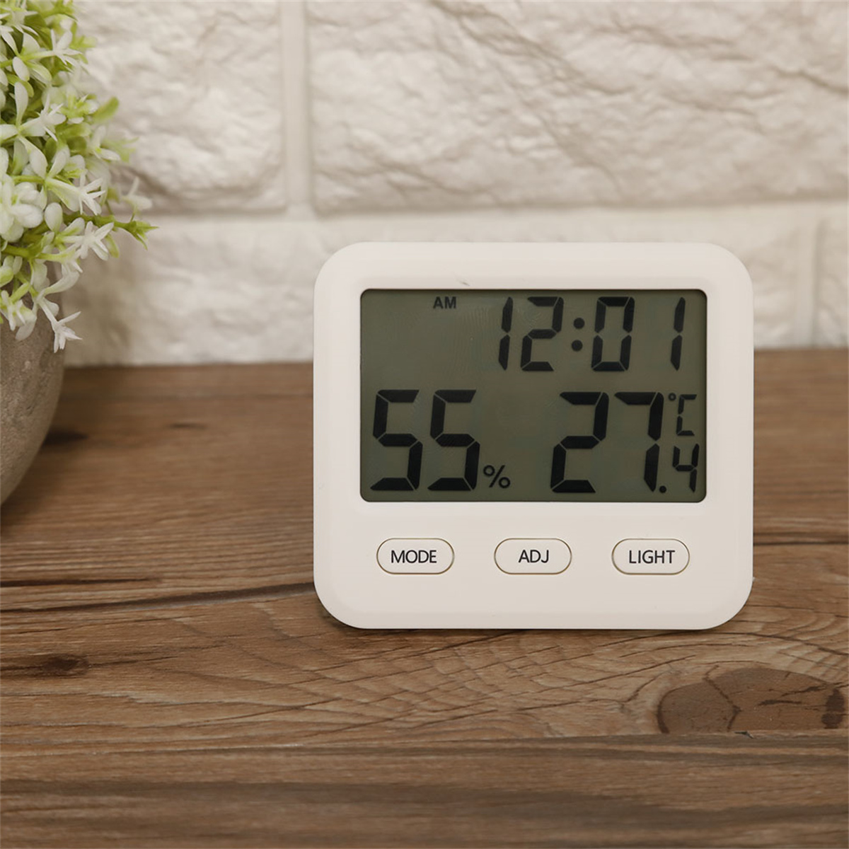 Weiße Digitaluhr, die Zeit, Luftfeuchtigkeit und Temperatur auf einer Holzoberfläche anzeigt.