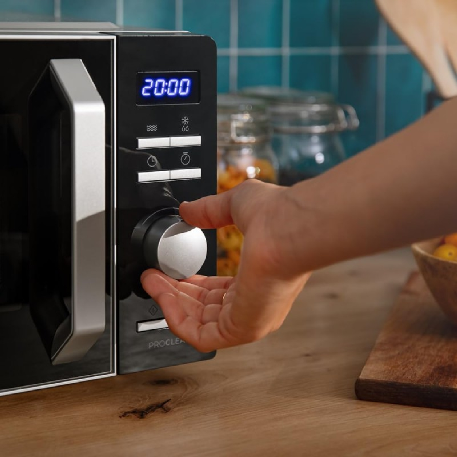 Una mano gira un quadrante su un forno a microonde nero in una cucina.