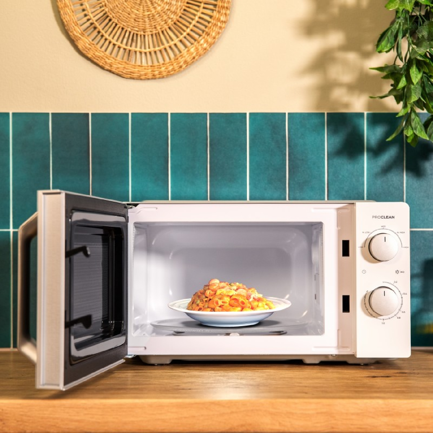 Een witte magnetron met de deur open, met gekookt voedsel op een bord erin. De achtergrond is een keuken.