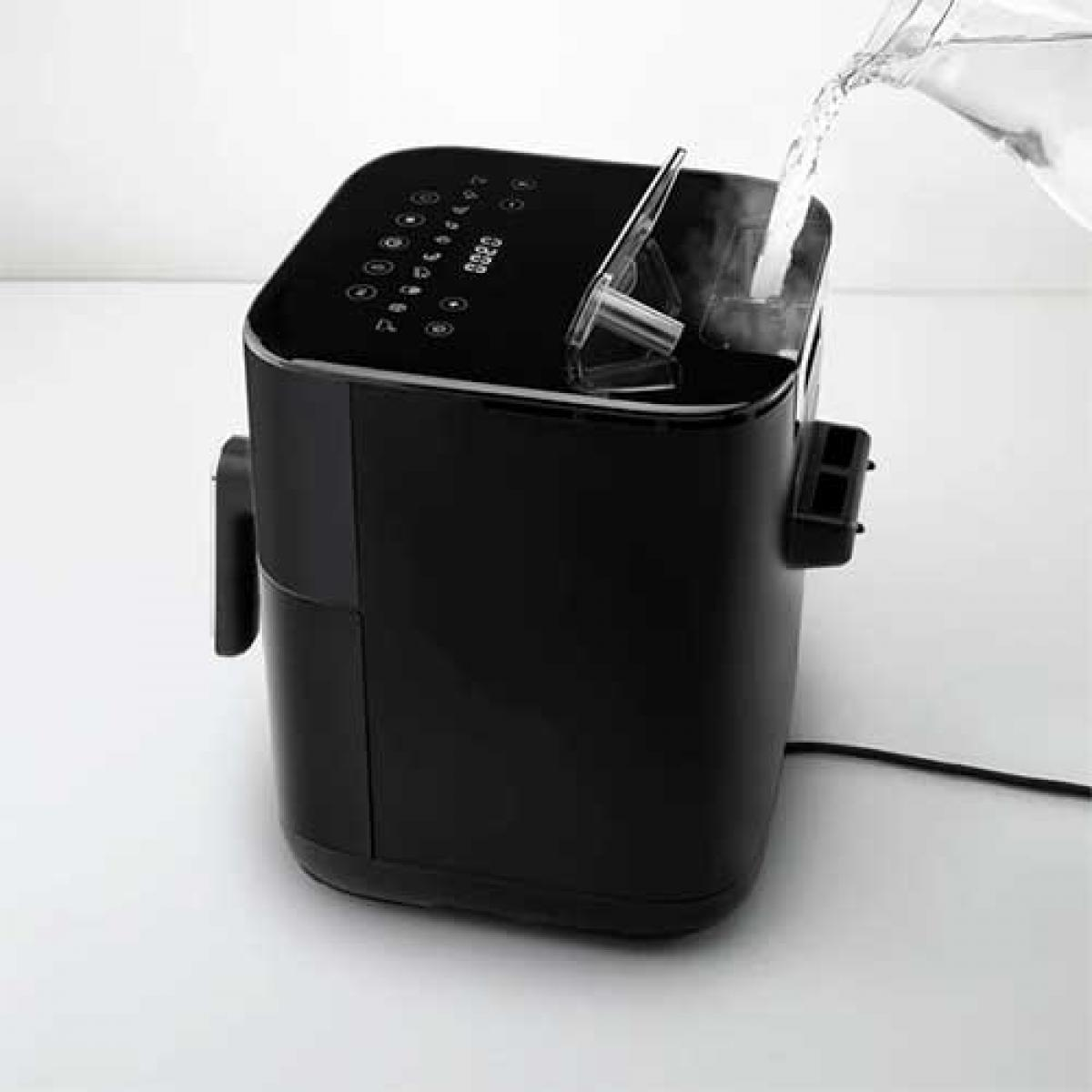 Czarna frytkownica powietrzna, do której wlewana jest woda z przezroczystego dzbanka.
