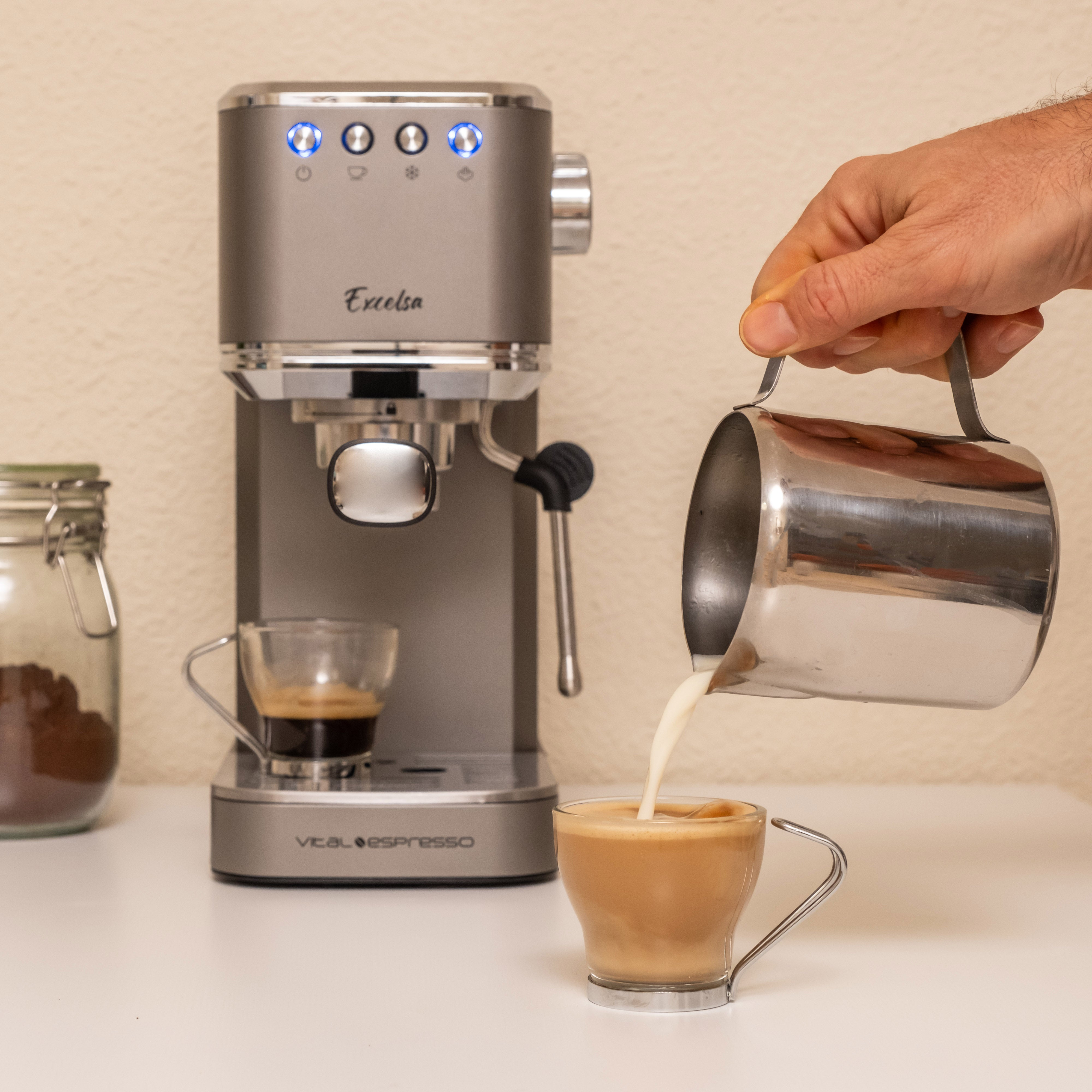 Alguien vierte leche en una taza de café con espresso, junto a una máquina de espresso gris.
