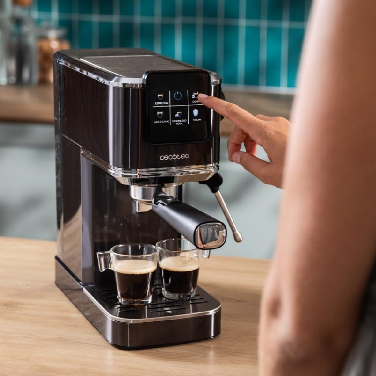 Ekspres do espresso z dwoma filiżankami kawy, ręka naciska przycisk, stylowy design.