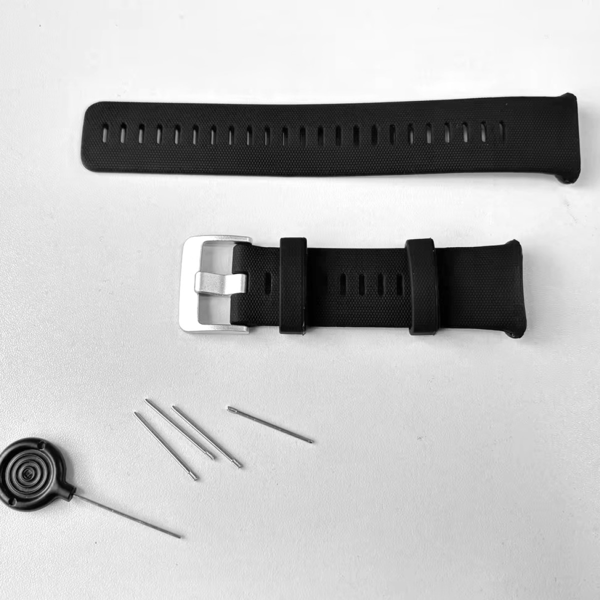 Czarne paski do zegarka, srebrna klamra i szpilki na białej powierzchni.