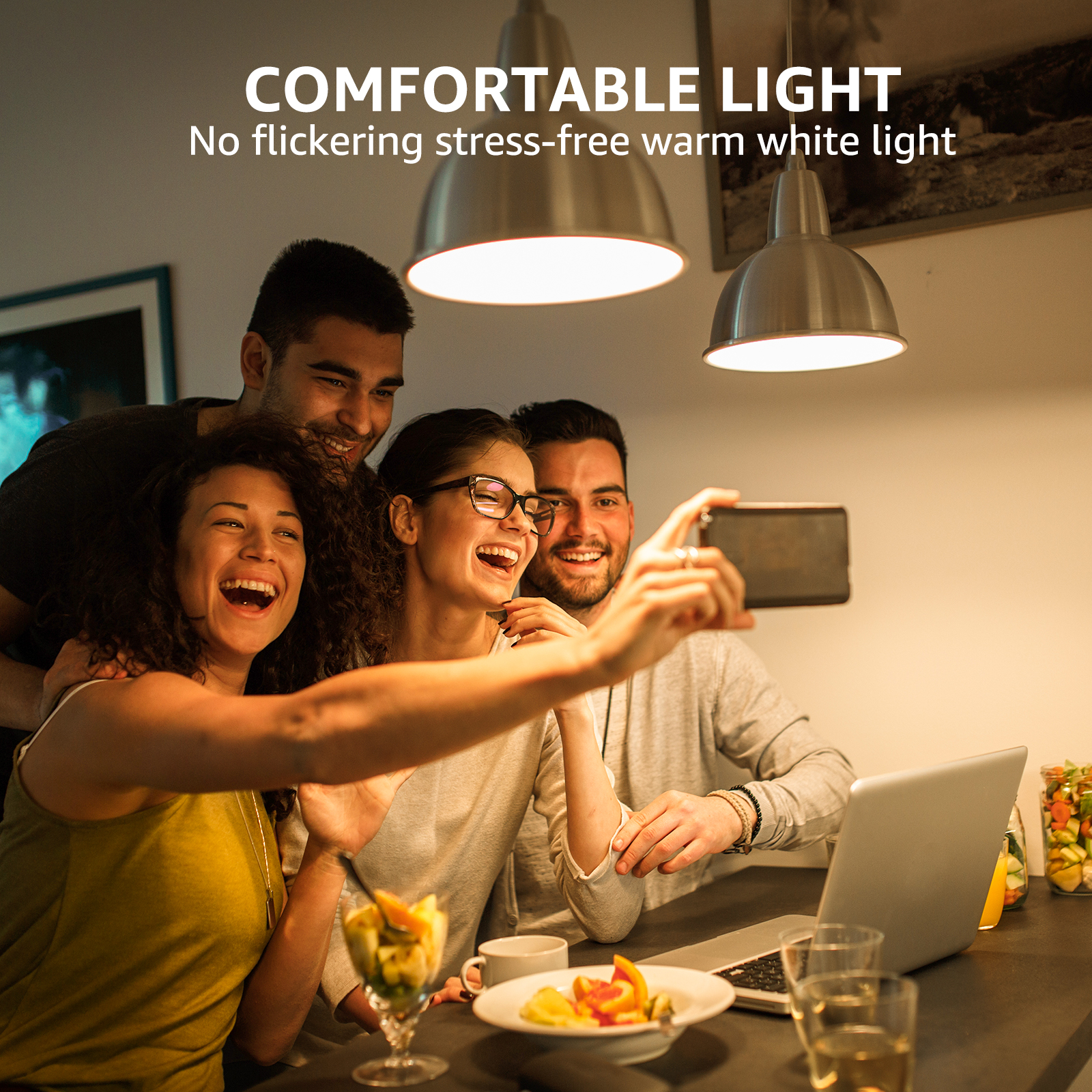 Quattro persone sorridenti che fanno un selfie sotto lampade a sospensione in un ambiente domestico.