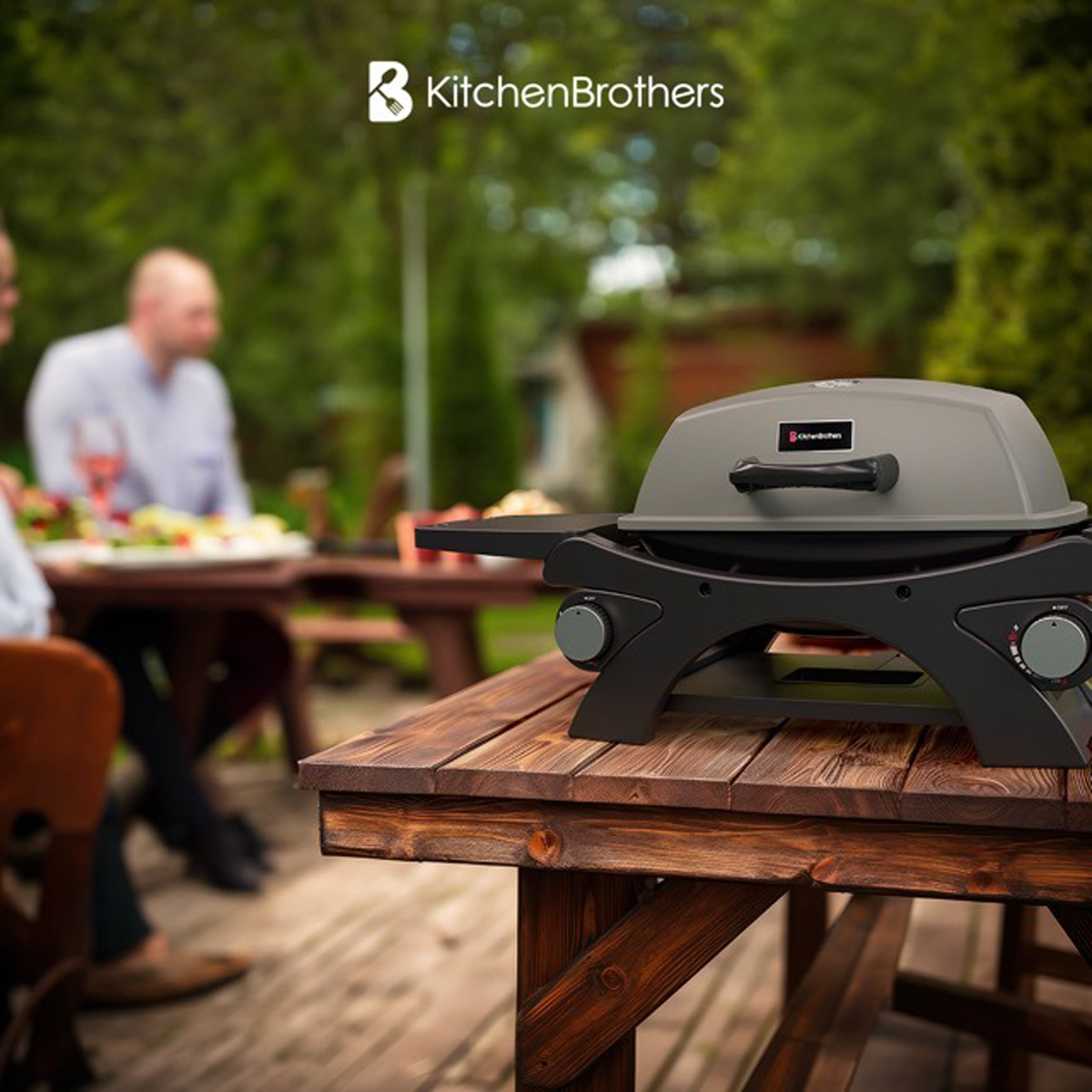 A small outdoor grill on a wooden table, with people blurred in the background enjoying a meal.