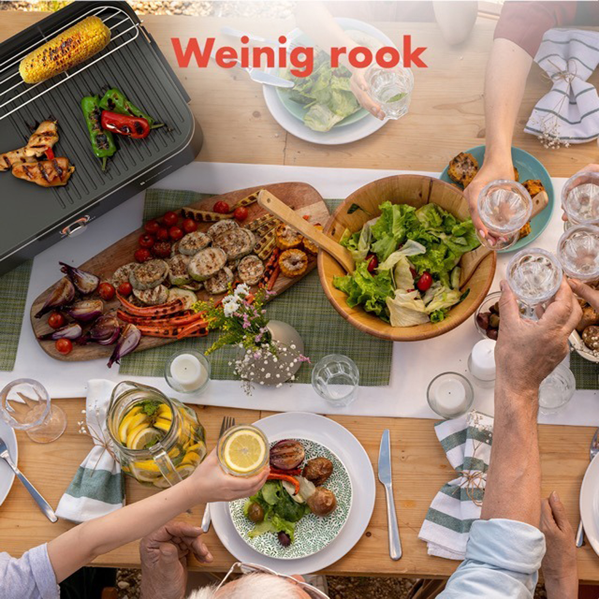 People at a table with food and drinks, grilled corn, vegetables, salad and glasses of water.