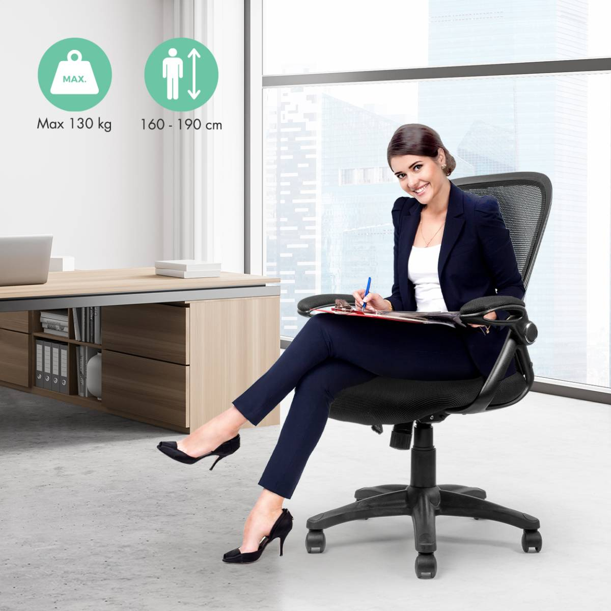 Woman in a business suit sits in an office chair. She's writing on a clipboard. Office setting.
