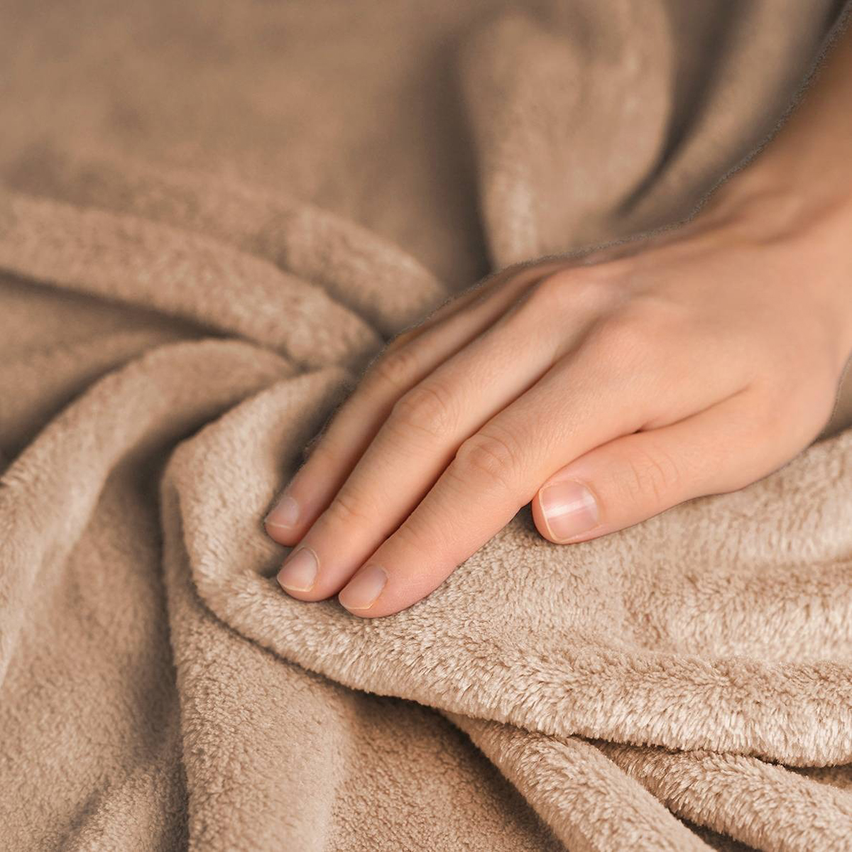 A hand touches a soft, beige blanket.