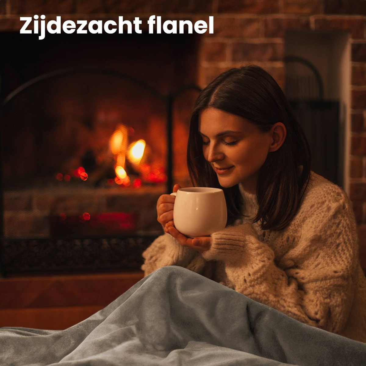 A woman in a sweater and a blanket, sitting by a fireplace holding a mug.