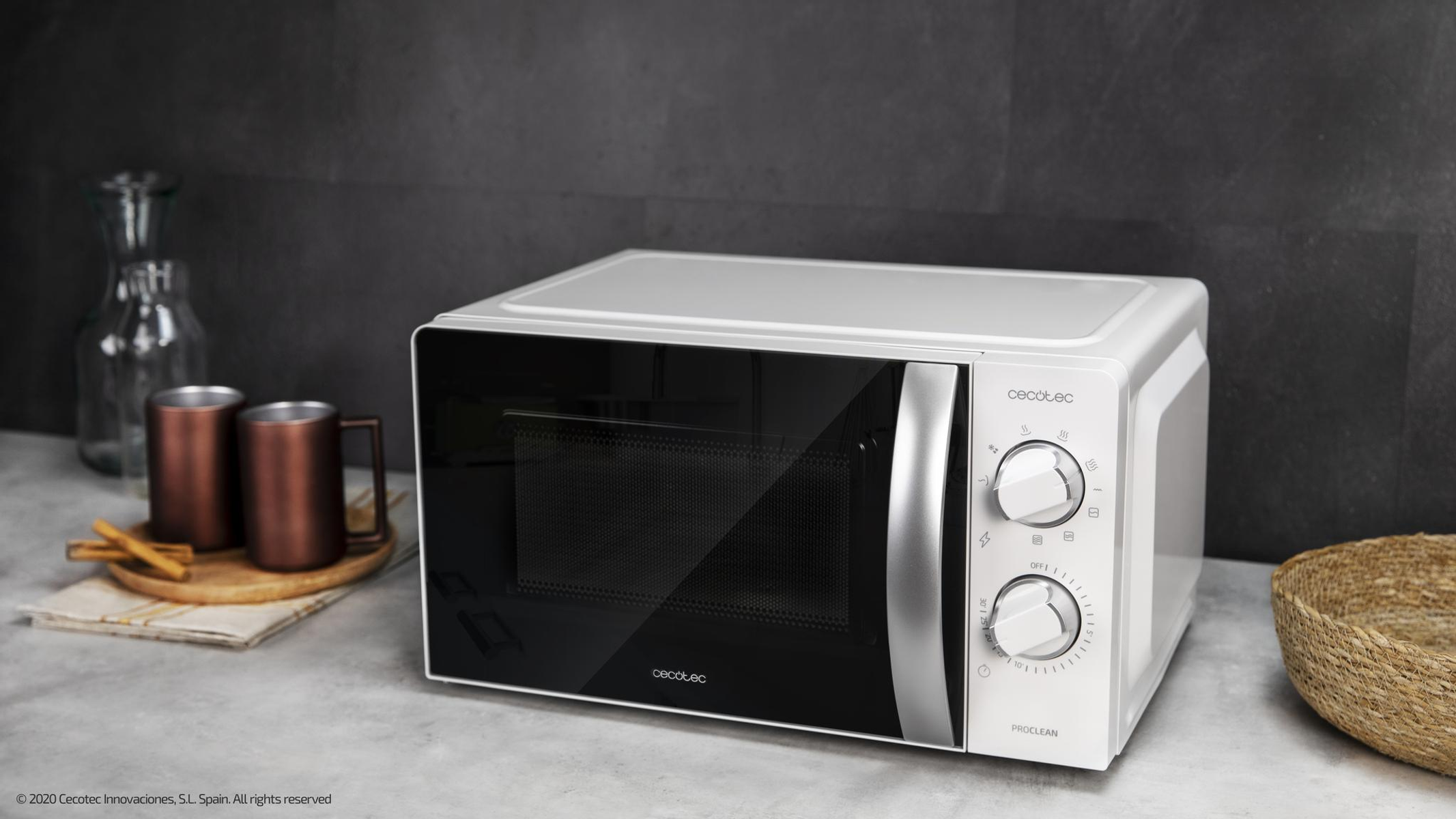 Biała i szara kuchenka mikrofalowa na blacie z ciemnym tłem. Są kubki i dekoracje.