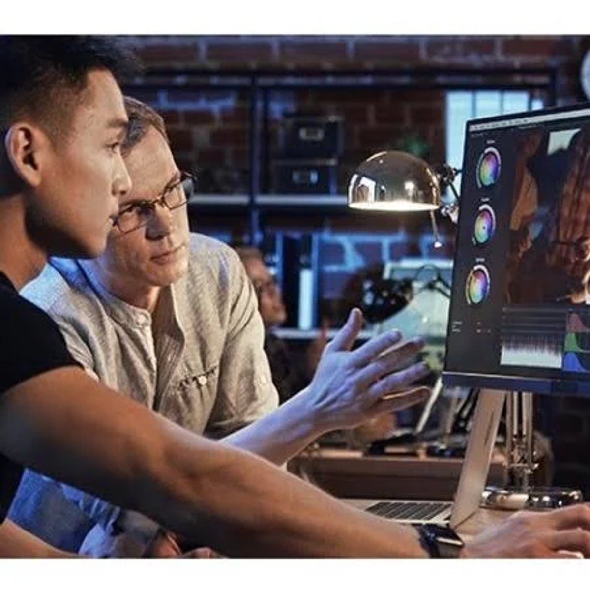 Dwóch mężczyzn w studio edytuje wideo na ekranie. Ekran pokazuje kolorowy interfejs edycji.