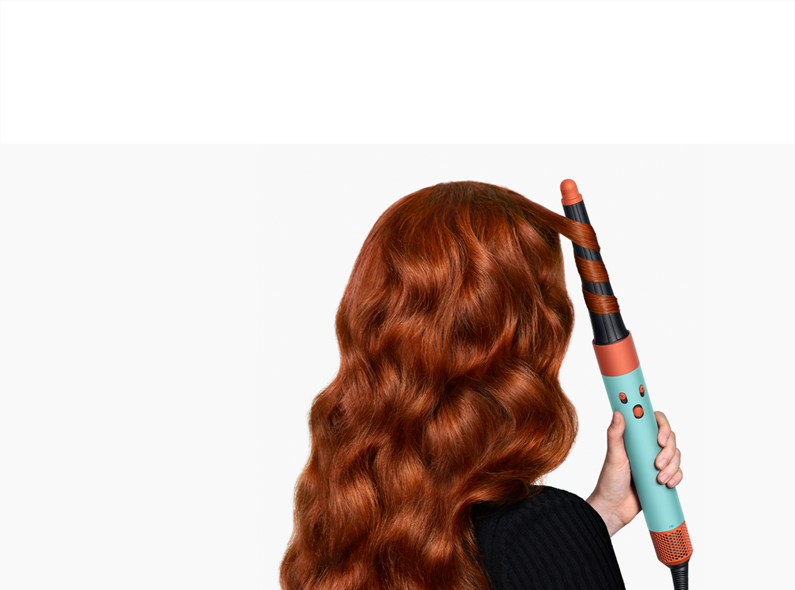 Osoba kręci czerwone włosy lokówką. Lokówka jest niebieska i pomarańczowa.