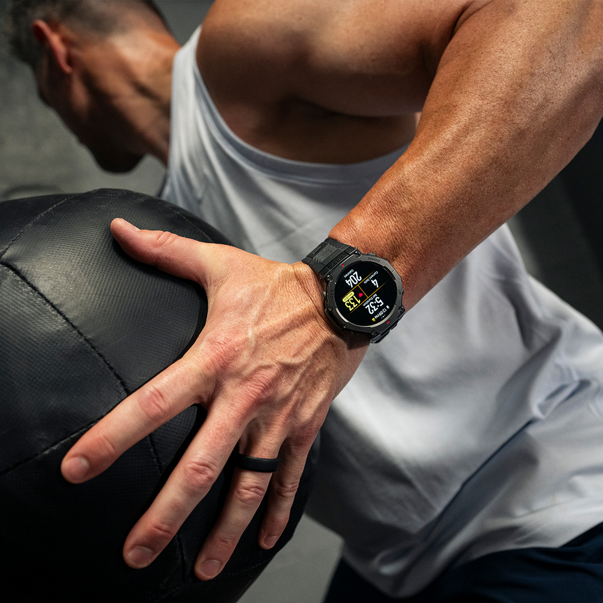 Mężczyzna noszący smartwatch, trzymający czarną piłkę lekarską, ćwiczący.