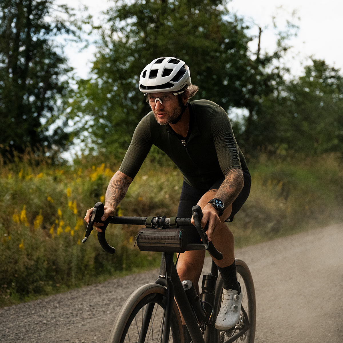 Kolarz na żwirowej drodze, w kasku, okularach i odzieży kolarskiej.