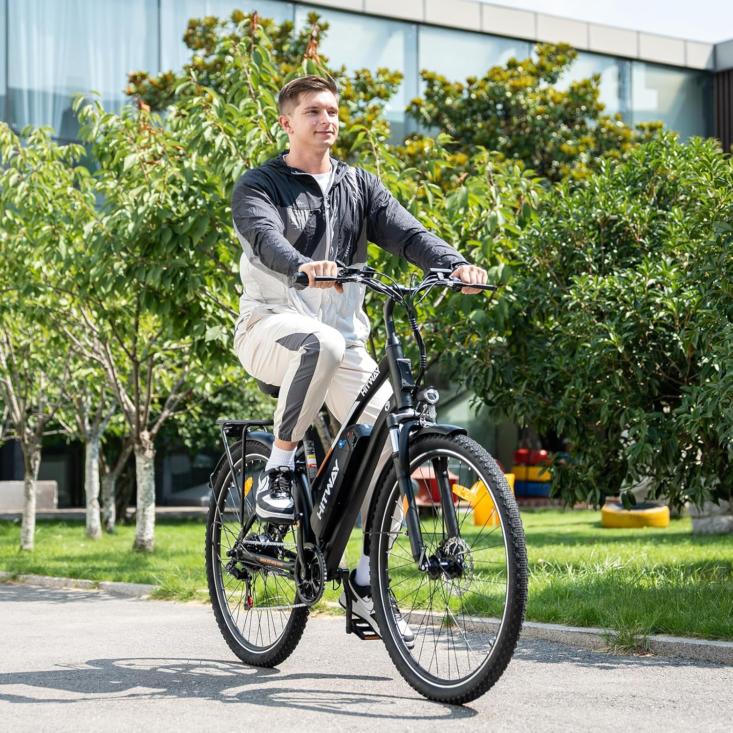 Mężczyzna jedzie czarnym rowerem elektrycznym po utwardzonej ścieżce. W tle drzewa i budynki.