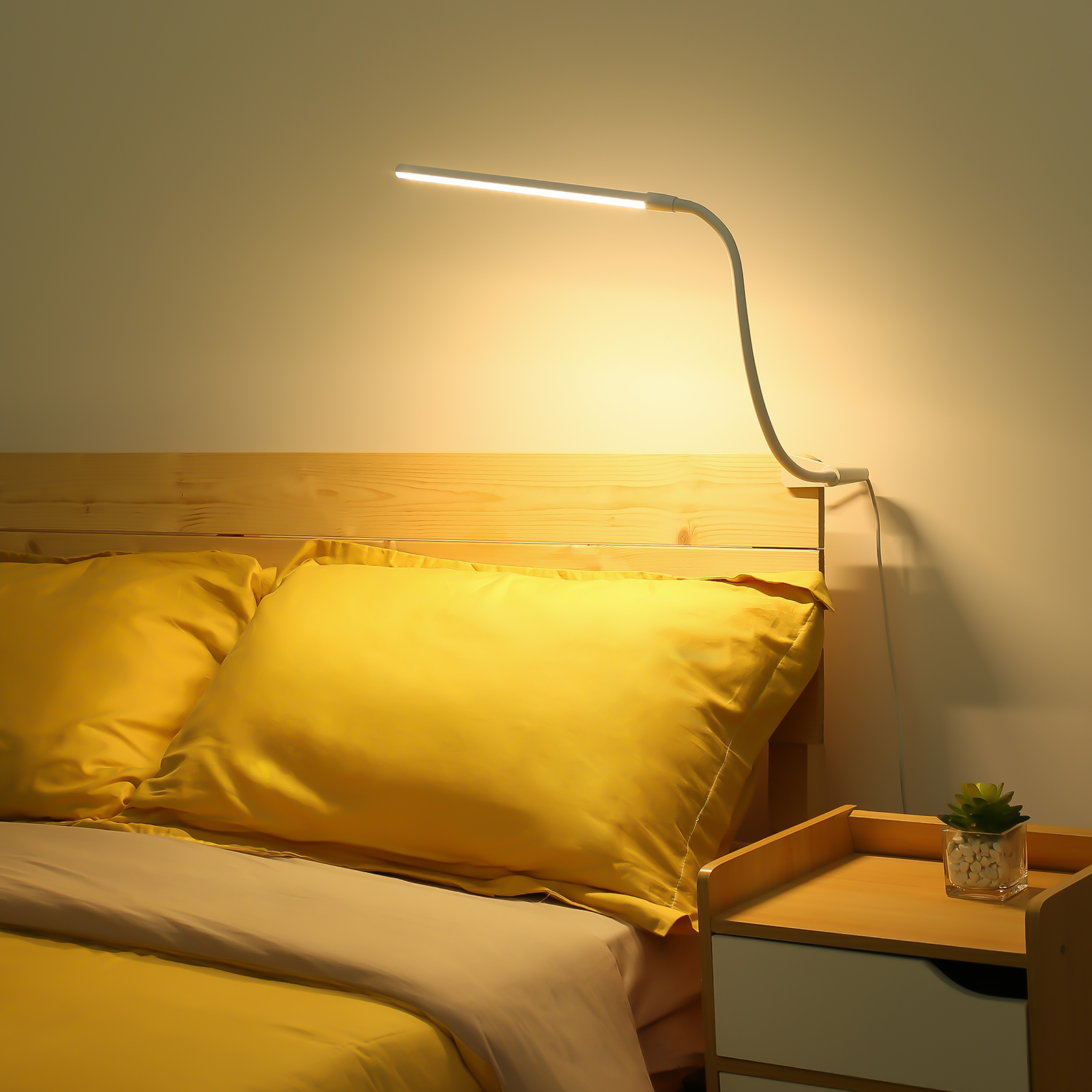 Eine weiße Schreibtischlampe mit flexiblem Hals leuchtet und beleuchtet ein Bett mit gelben Kissen.