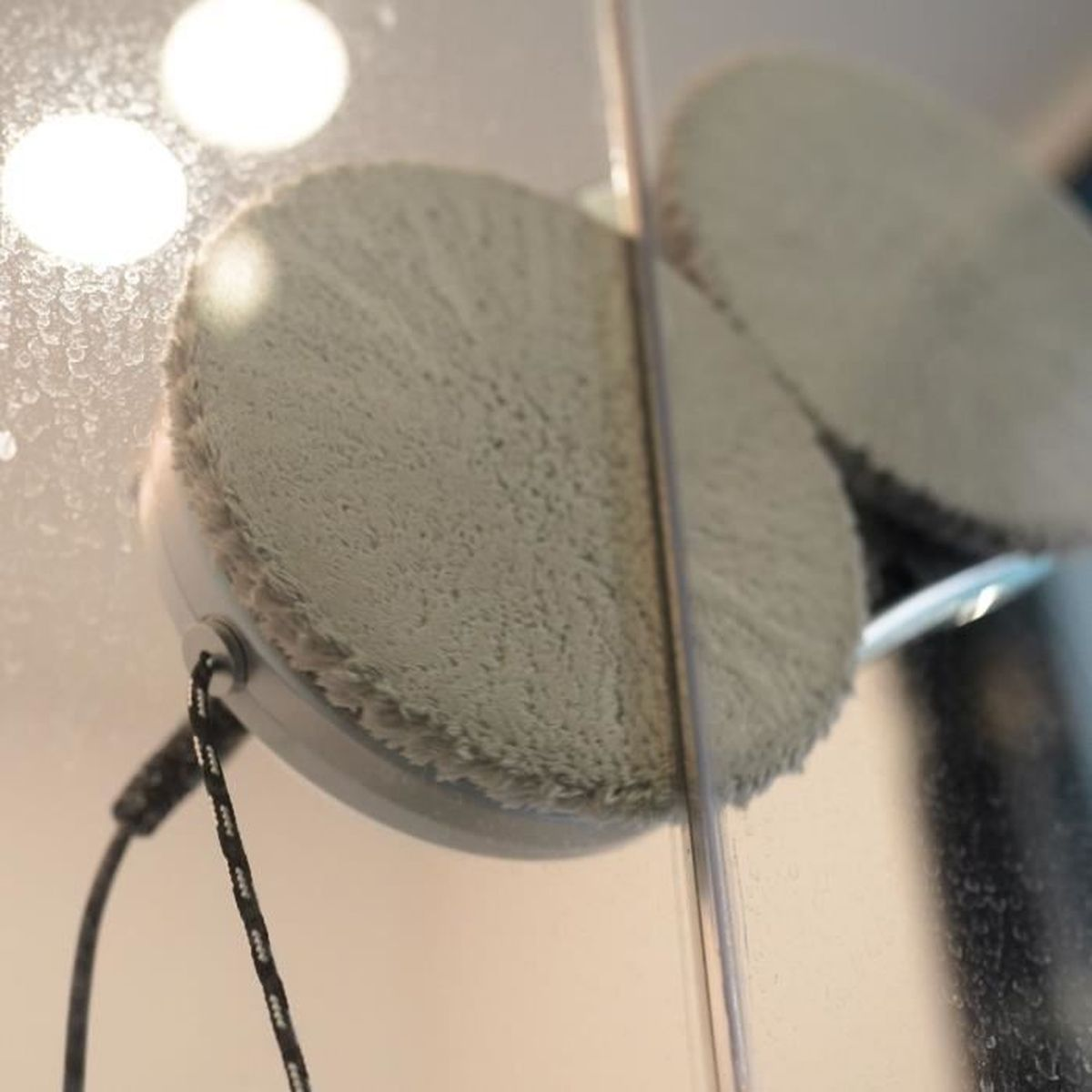 Okrągły, biały, zmotoryzowany czyścik do okien z puszystą podkładką czyszczącą szklaną powierzchnię.