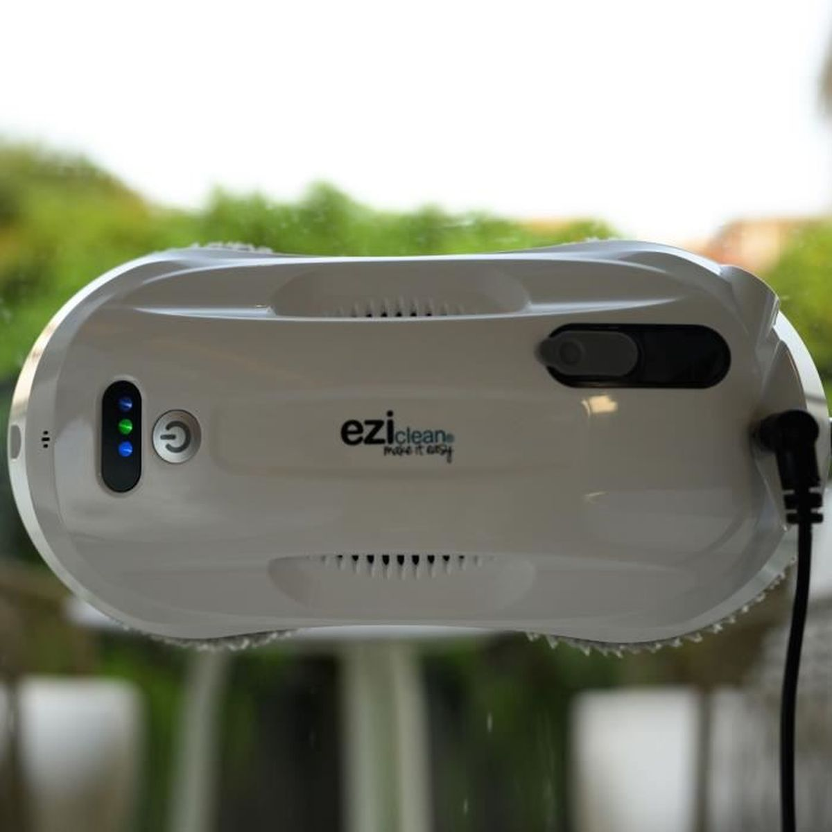 Biały robot do czyszczenia okien na oknie, z zielonym tłem drzew.