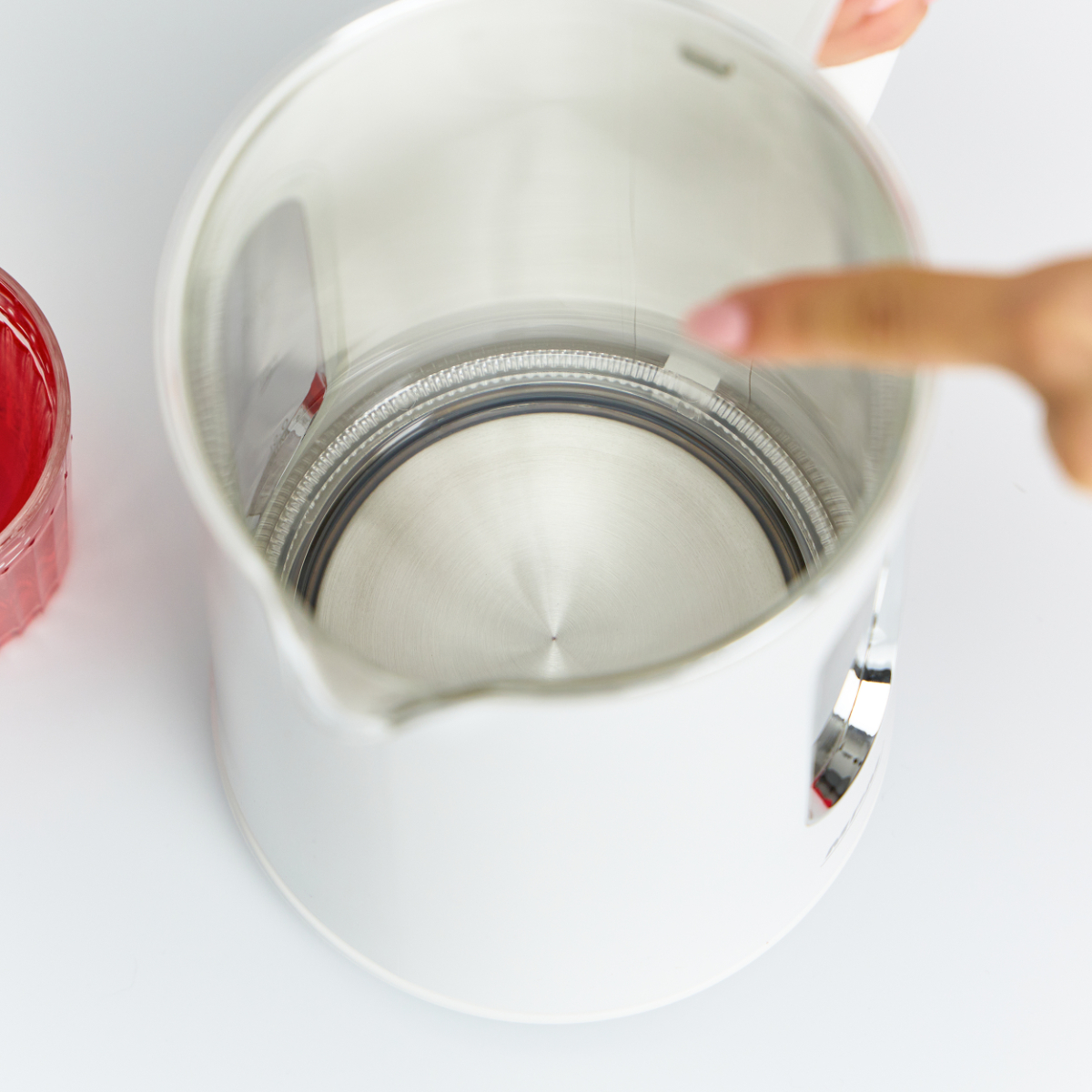 Interno del bollitore bianco. Una mano indica all'interno. Un bicchiere di liquido rosso a sinistra.