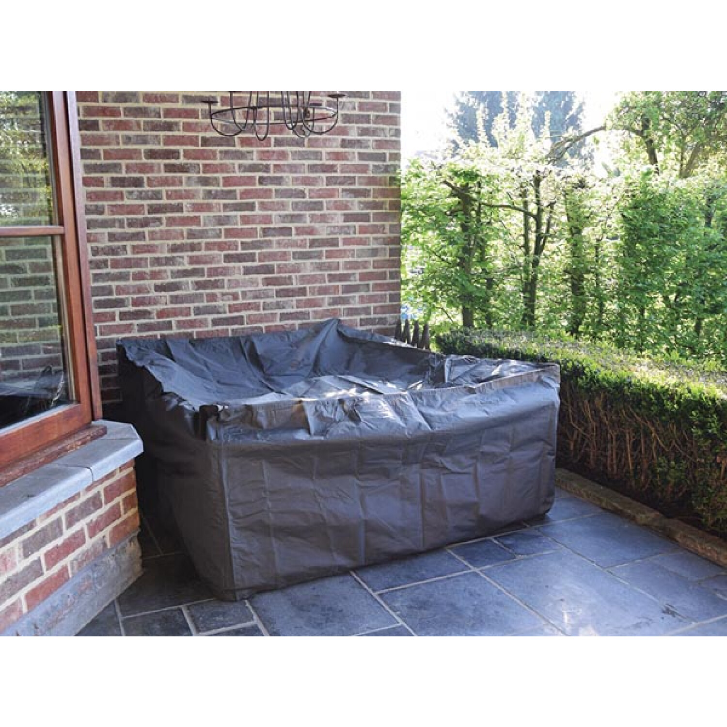 Ein abgedeckter Whirlpool steht auf einer Terrasse mit Backsteinmauer und Grün im Hintergrund.