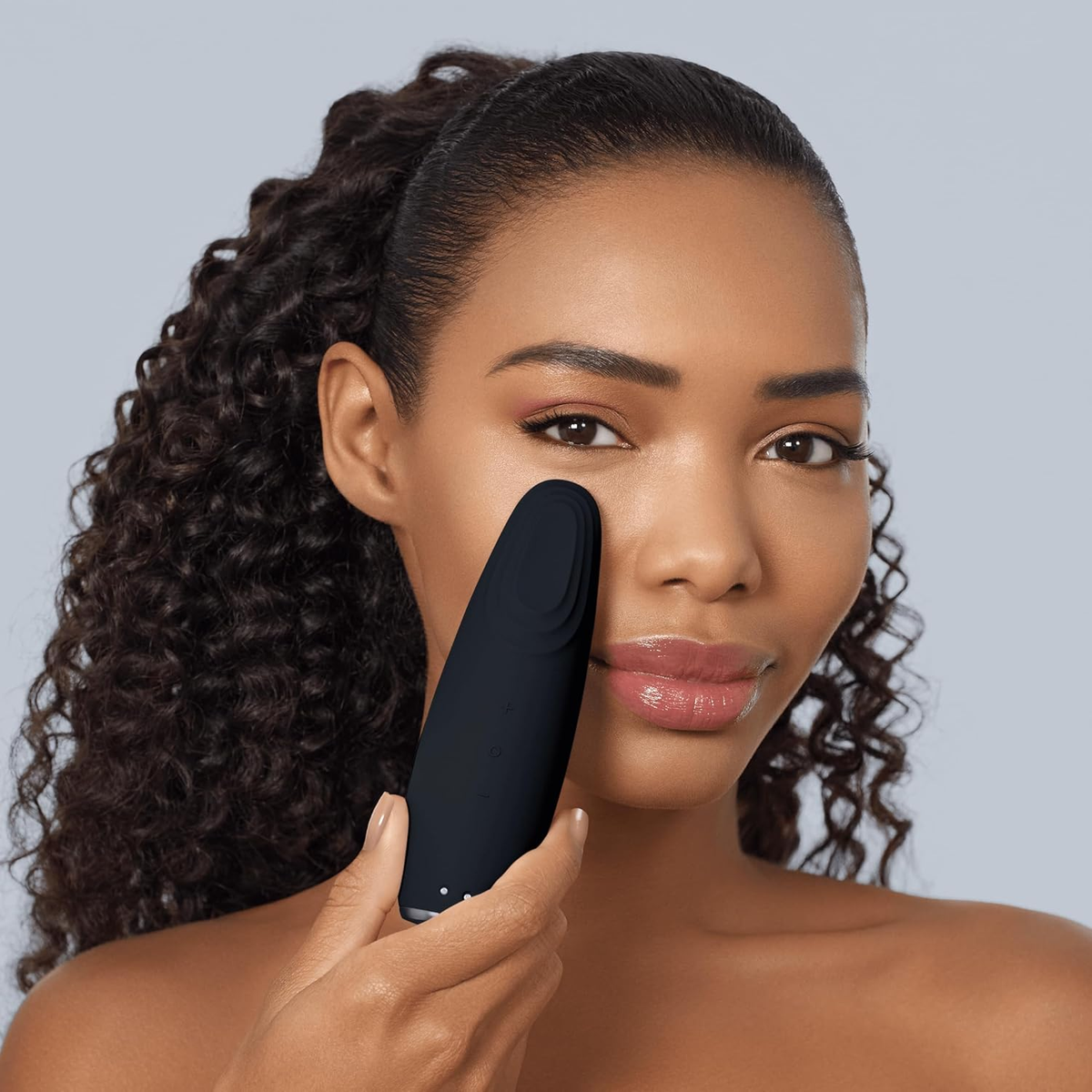 Una donna tiene un dispositivo nero sulla guancia. Ha i capelli scuri e guarda la fotocamera.