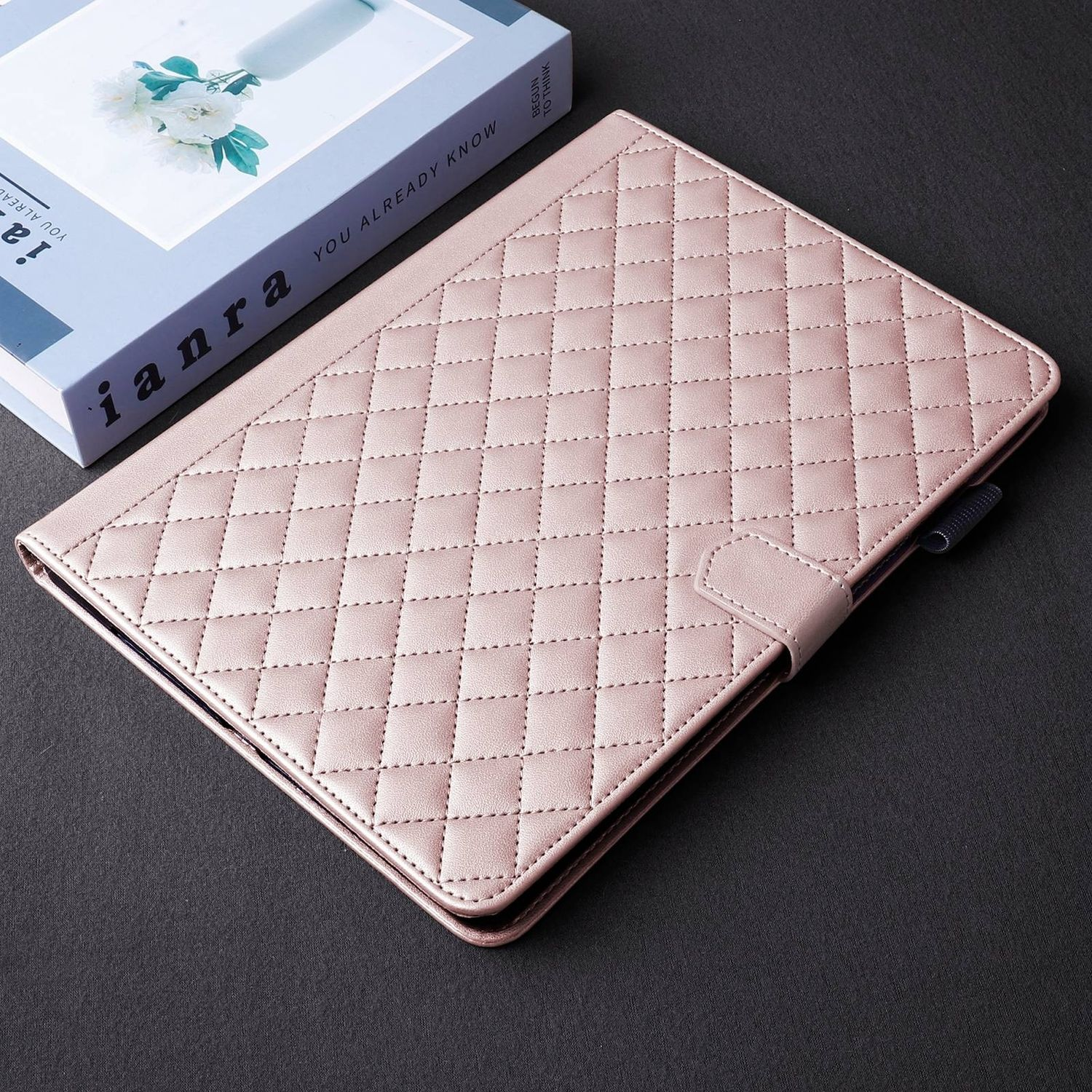 Eine rosa Tablethülle aus Leder mit Rautenmuster und Druckknopfverschluss, auf schwarzem Untergrund.