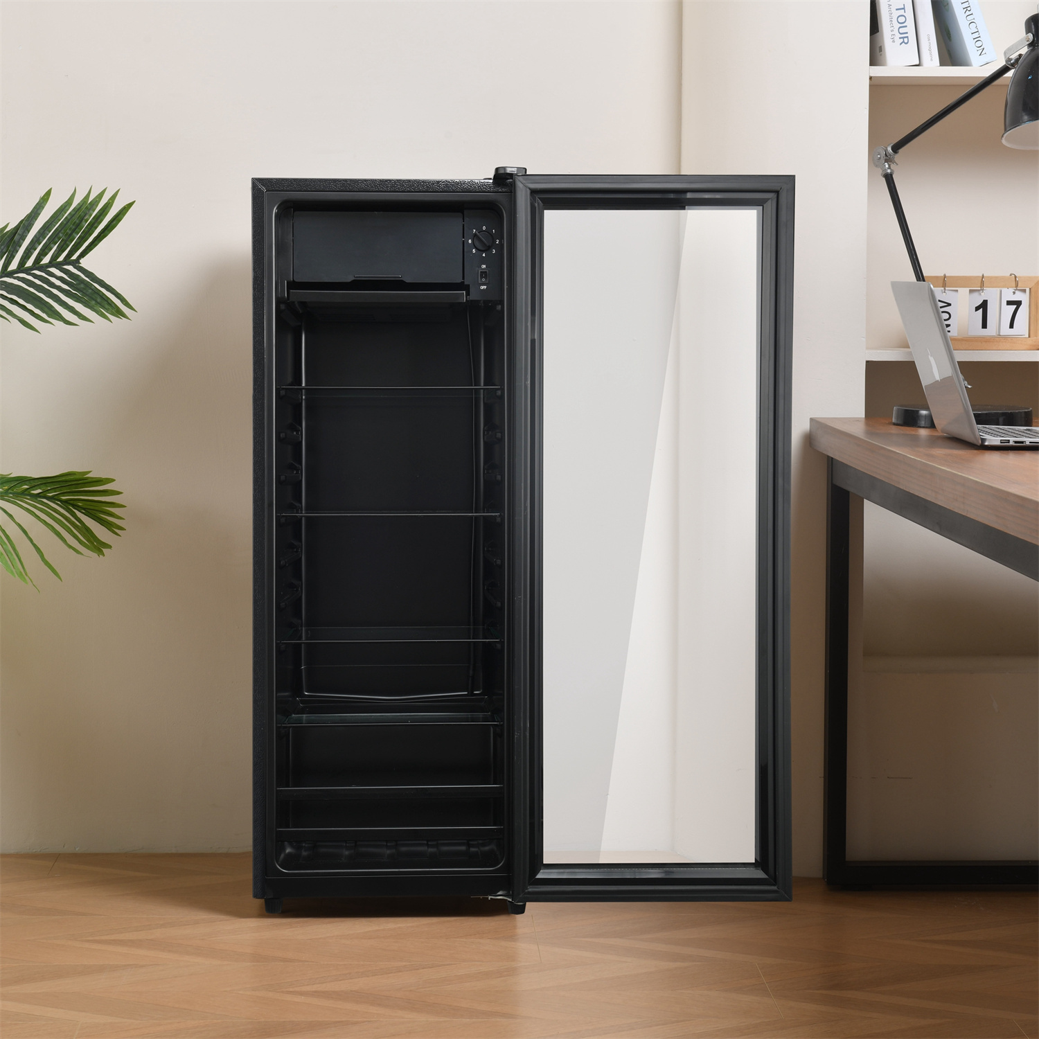 Schwarzer Weinkühlschrank mit offener Glastür. Regale im Inneren. Schreibtisch und Lampe im Hintergrund.