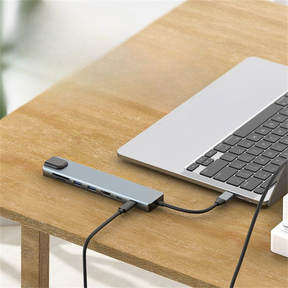 Ein silberner USB-Hub ist mit einem Laptop auf einem Holztisch verbunden. Kabel sind angeschlossen.