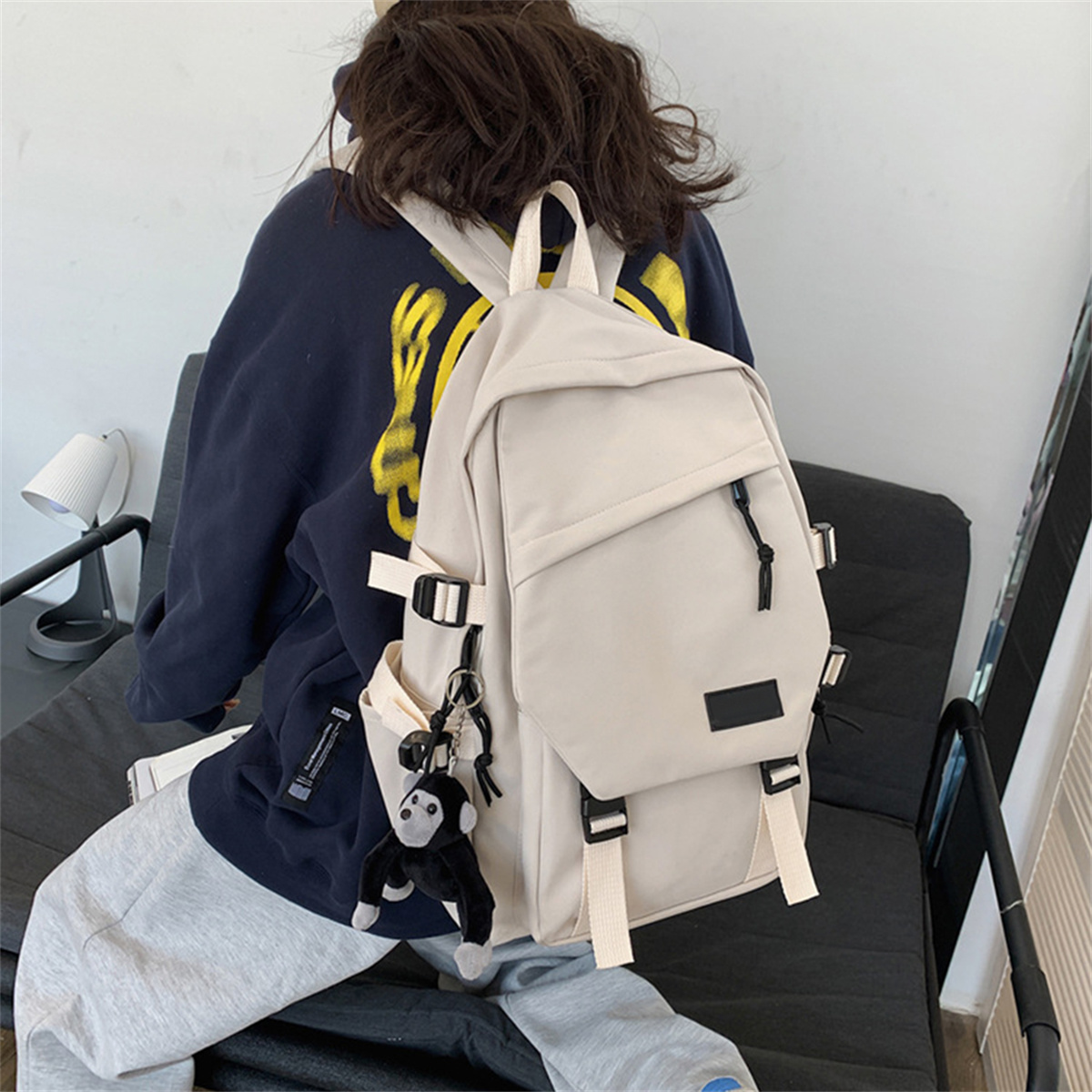 Person mit beigem Rucksack. Merkmale sind Taschen, schwarze Riemen und ein Affen-Schlüsselanhänger.