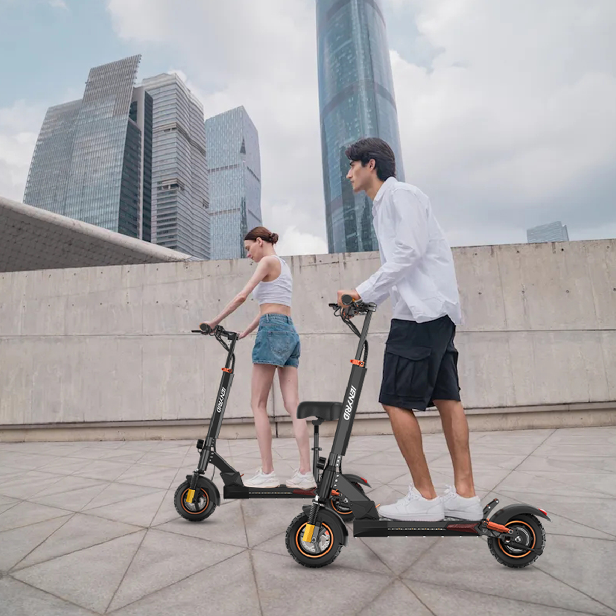 Due persone in sella a scooter elettrici. Sfondo urbano, edifici e cielo nuvoloso.