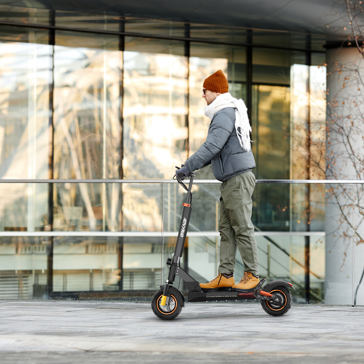 Uomo che guida uno scooter elettrico nero su un marciapiede. Edifici sullo sfondo.