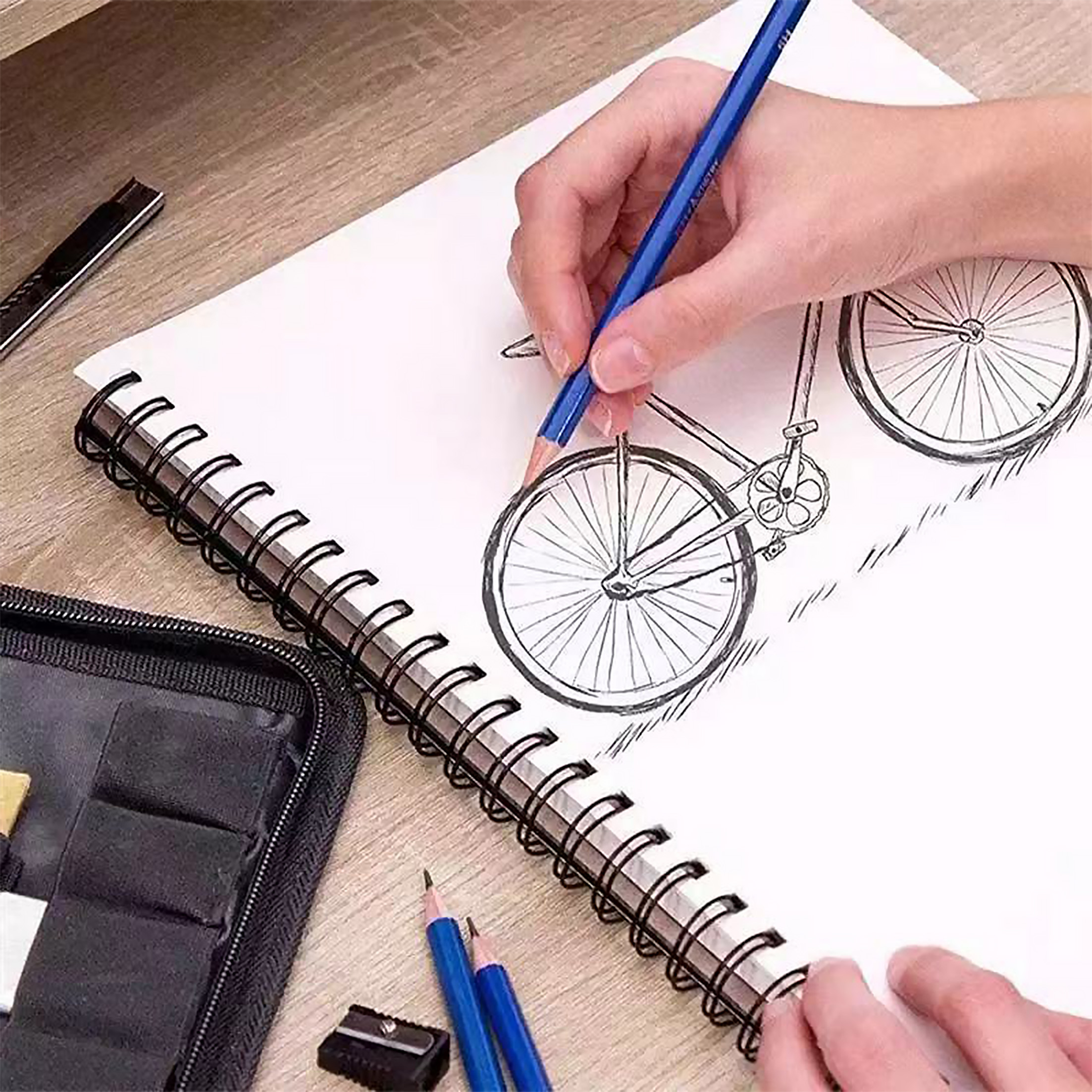 Person skizziert mit einem Bleistift ein Fahrrad auf einem Spiralblock.