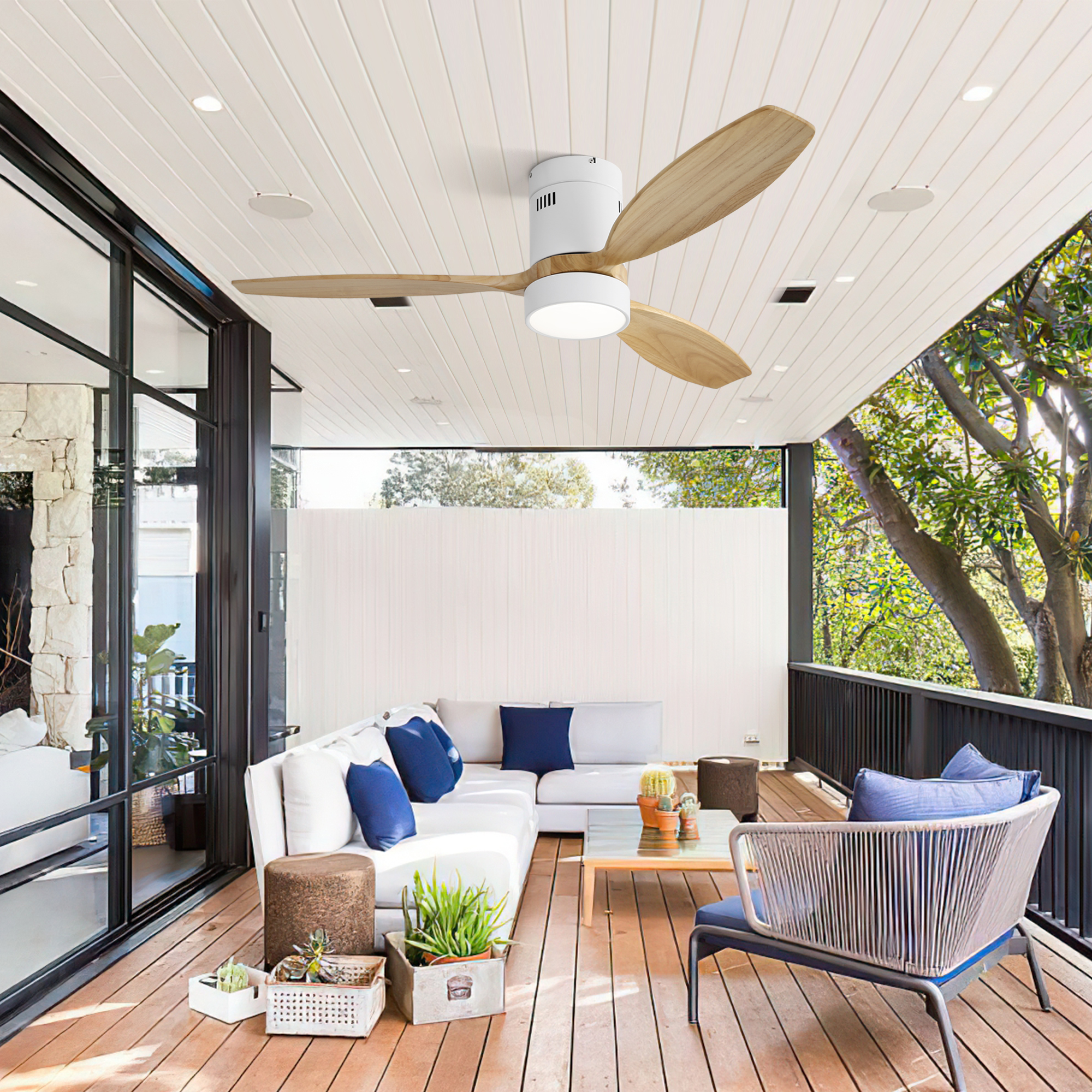 Außenbereich mit Deckenventilator, weißen Sofas und Holzterrasse. Grüne Bäume und Himmel im Hintergrund.