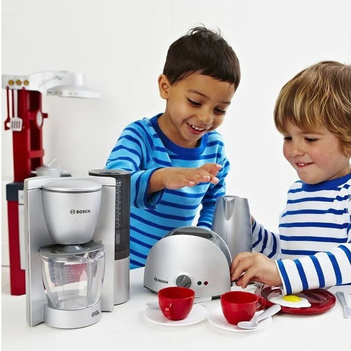 Zwei lächelnde Kinder spielen mit Spielzeug-Küchengeräten und Essen.