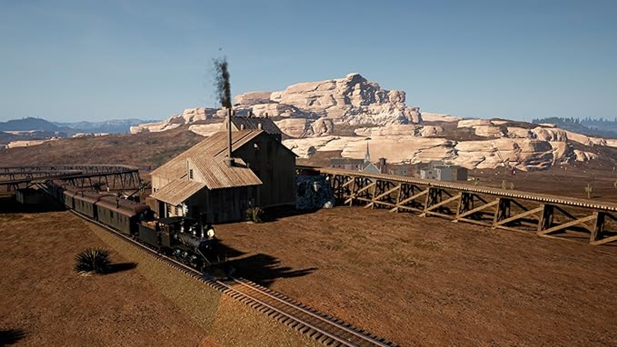 Un tren que viaja por un paisaje desértico con un puente de madera y un pueblo pequeño.