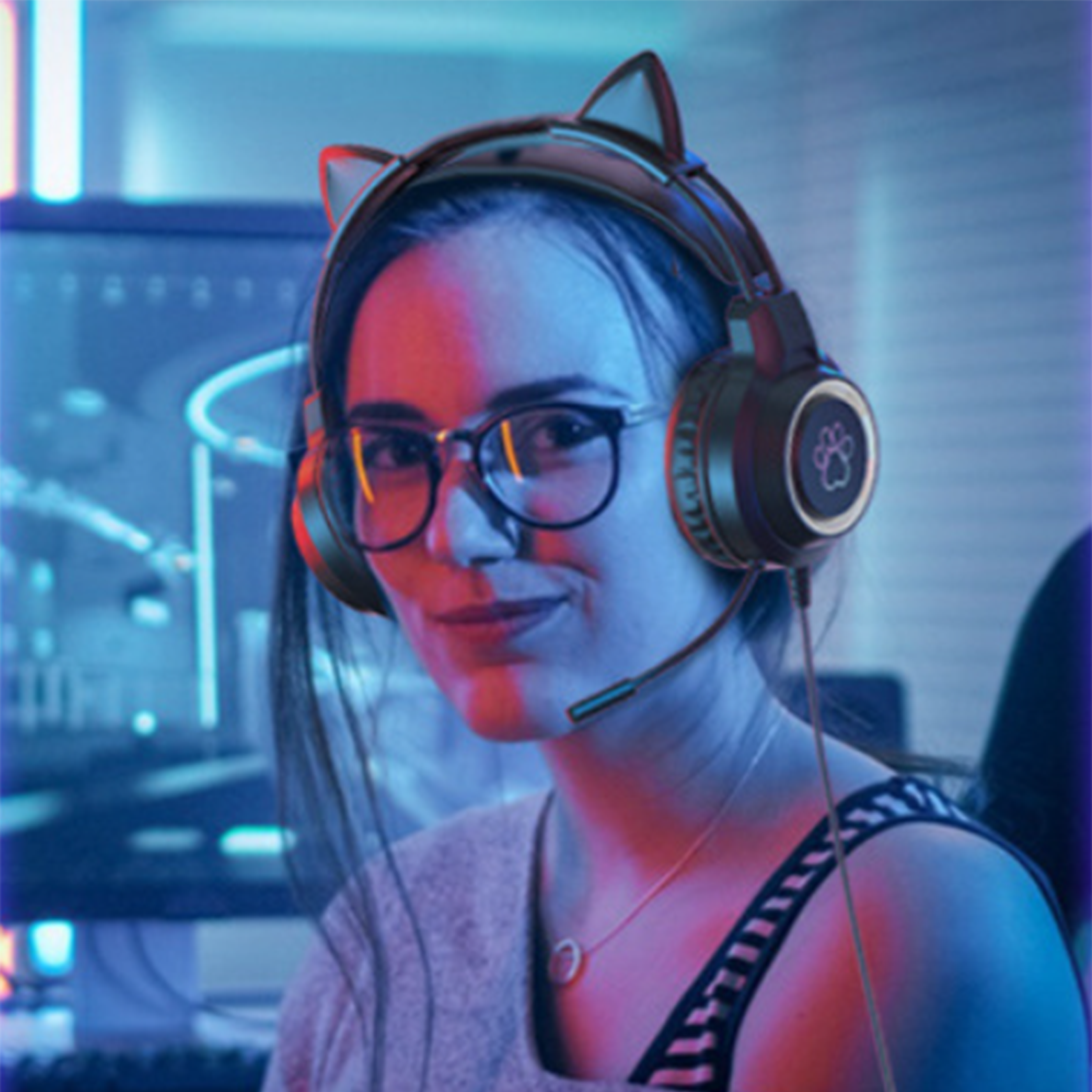 Eine Frau mit Brille und Headset mit Katzenohren lächelt. Der Hintergrund hat rote und blaue Beleuchtung.